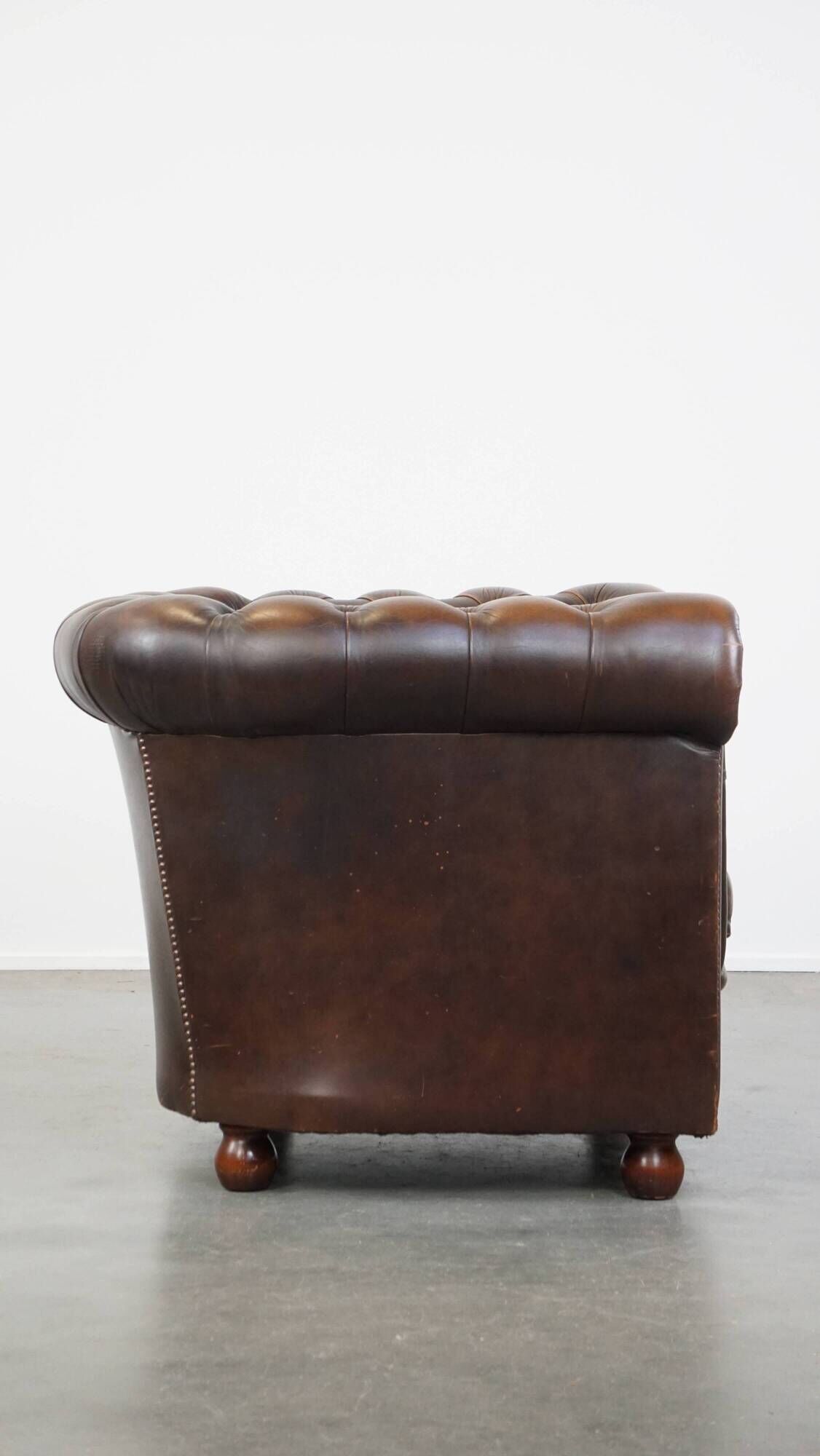 Cowhide English Chesterfield armchair with ball legs and timeless finish