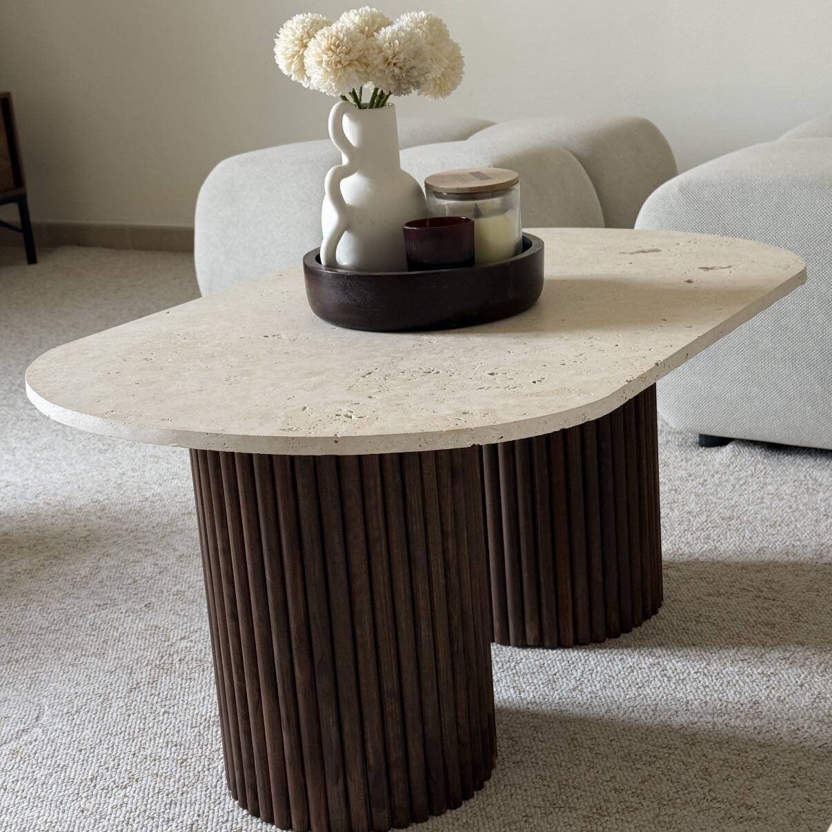 Oval coffee table in travertine and fluted wood.