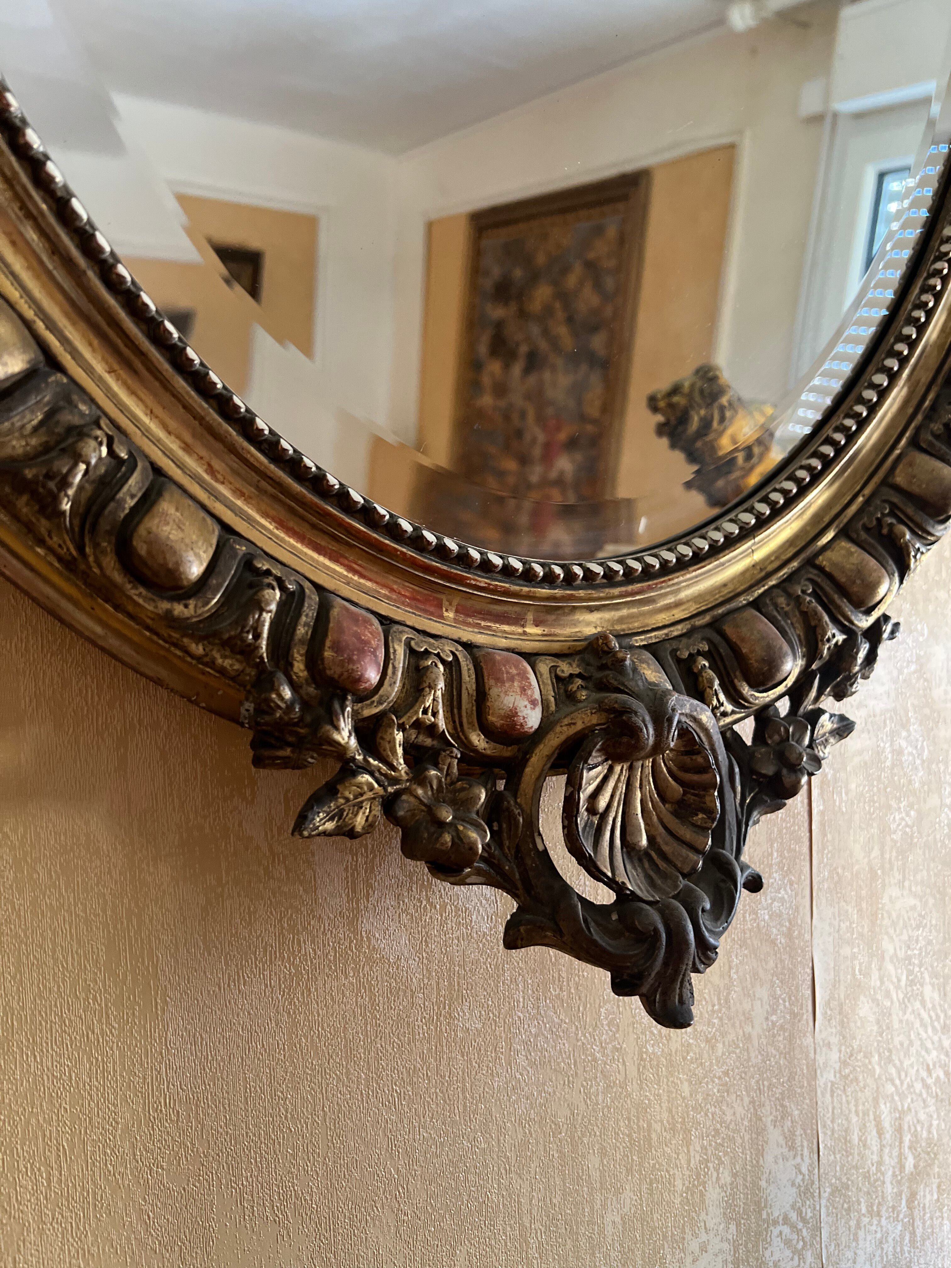 Antique oval mirror in gilded stucco with ornamentation