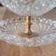 Two-tier display stand in cut glass mounted on a gold metal base.