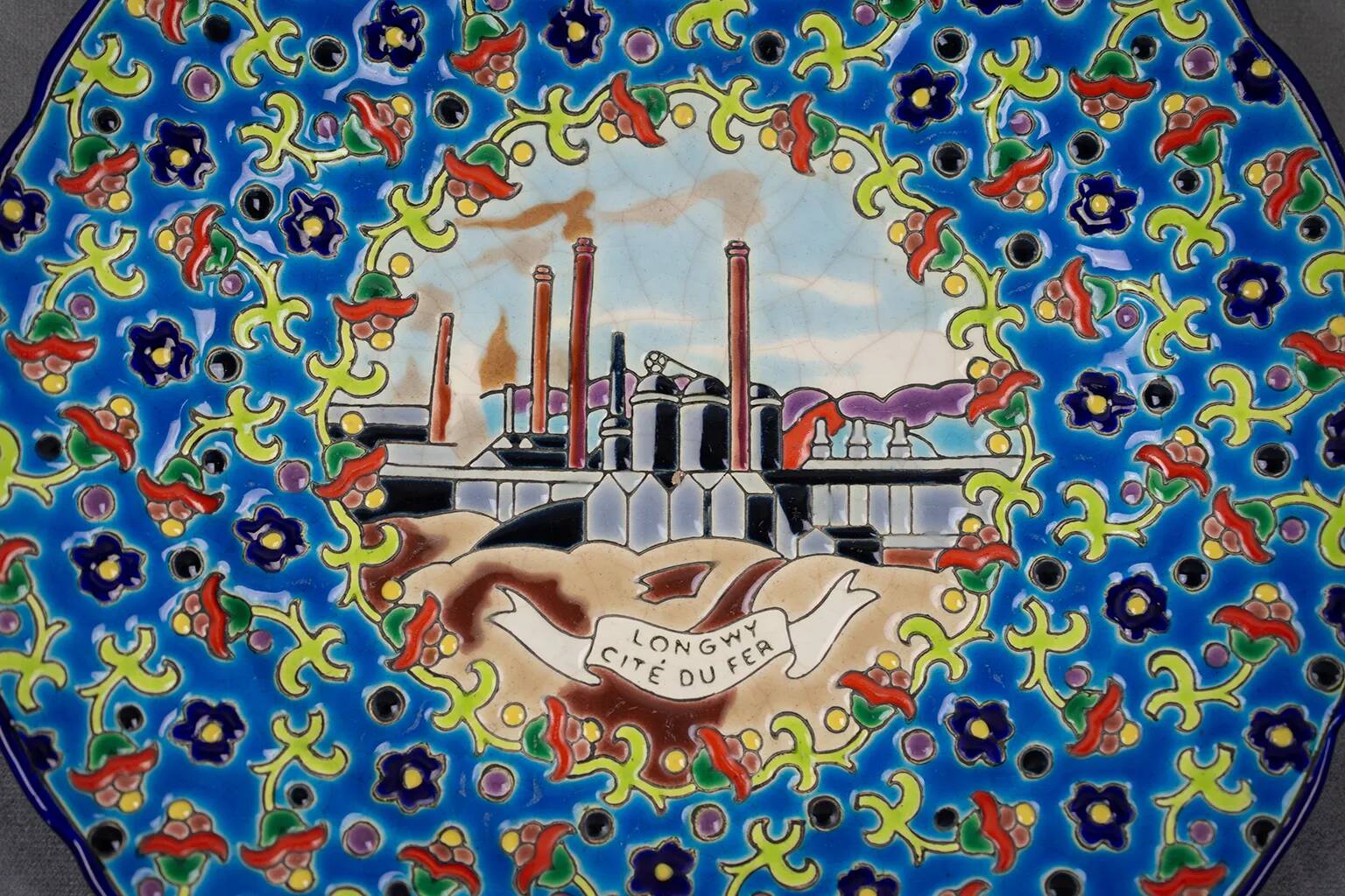 Longwy plate with polychrome enamels, decorated with the "City of Iron" motif.