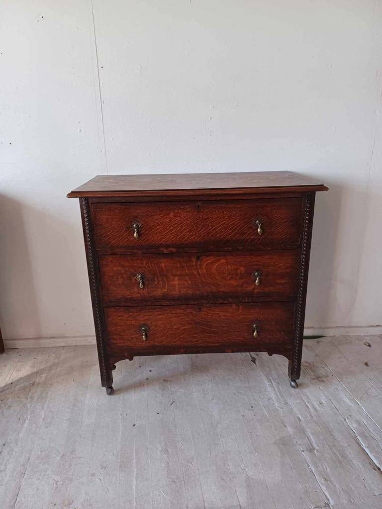 Antique oak chest of drawers on castors with brass handles and carved details