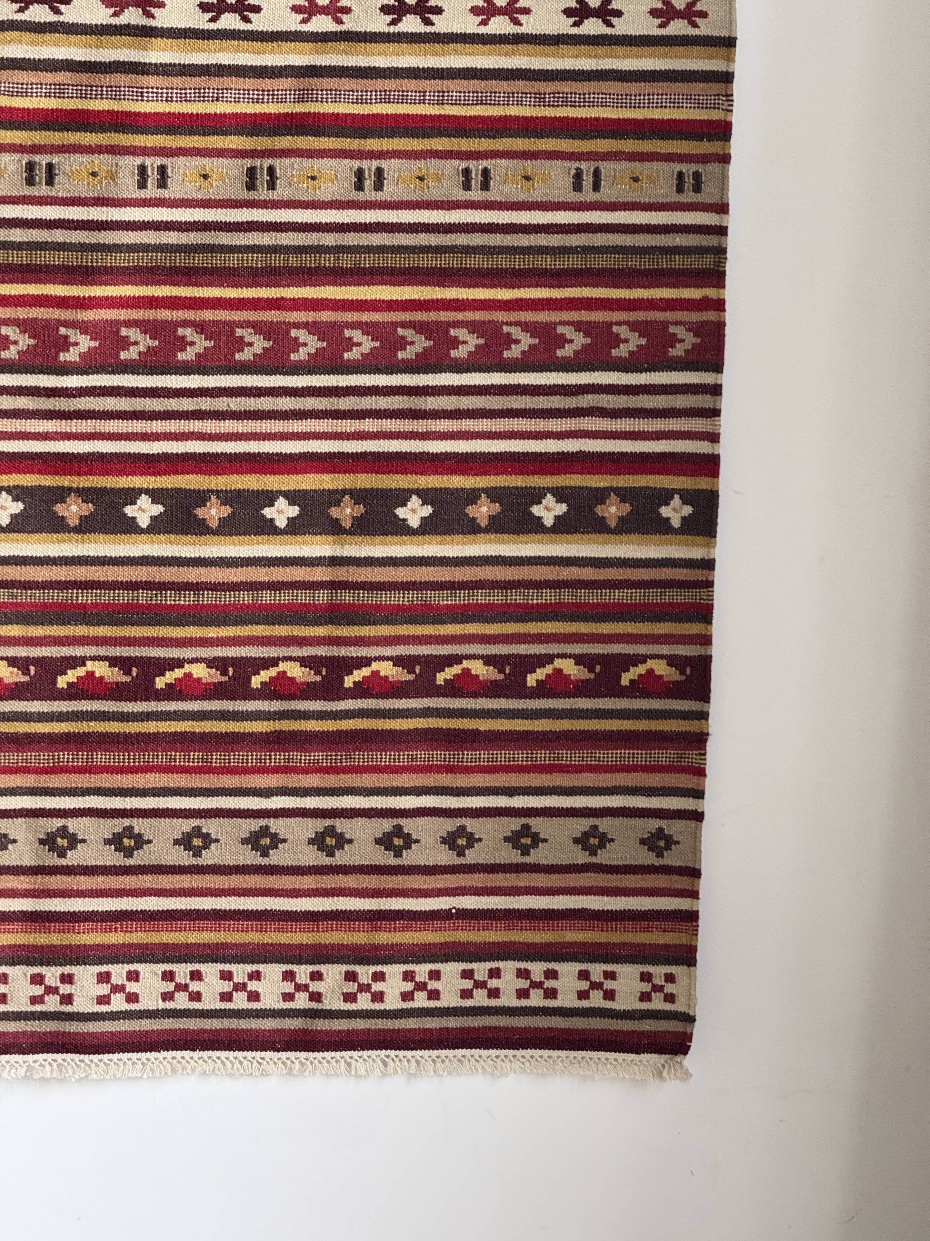 Large Indian rug with red, yellow, and white stripes and geometric fringes.