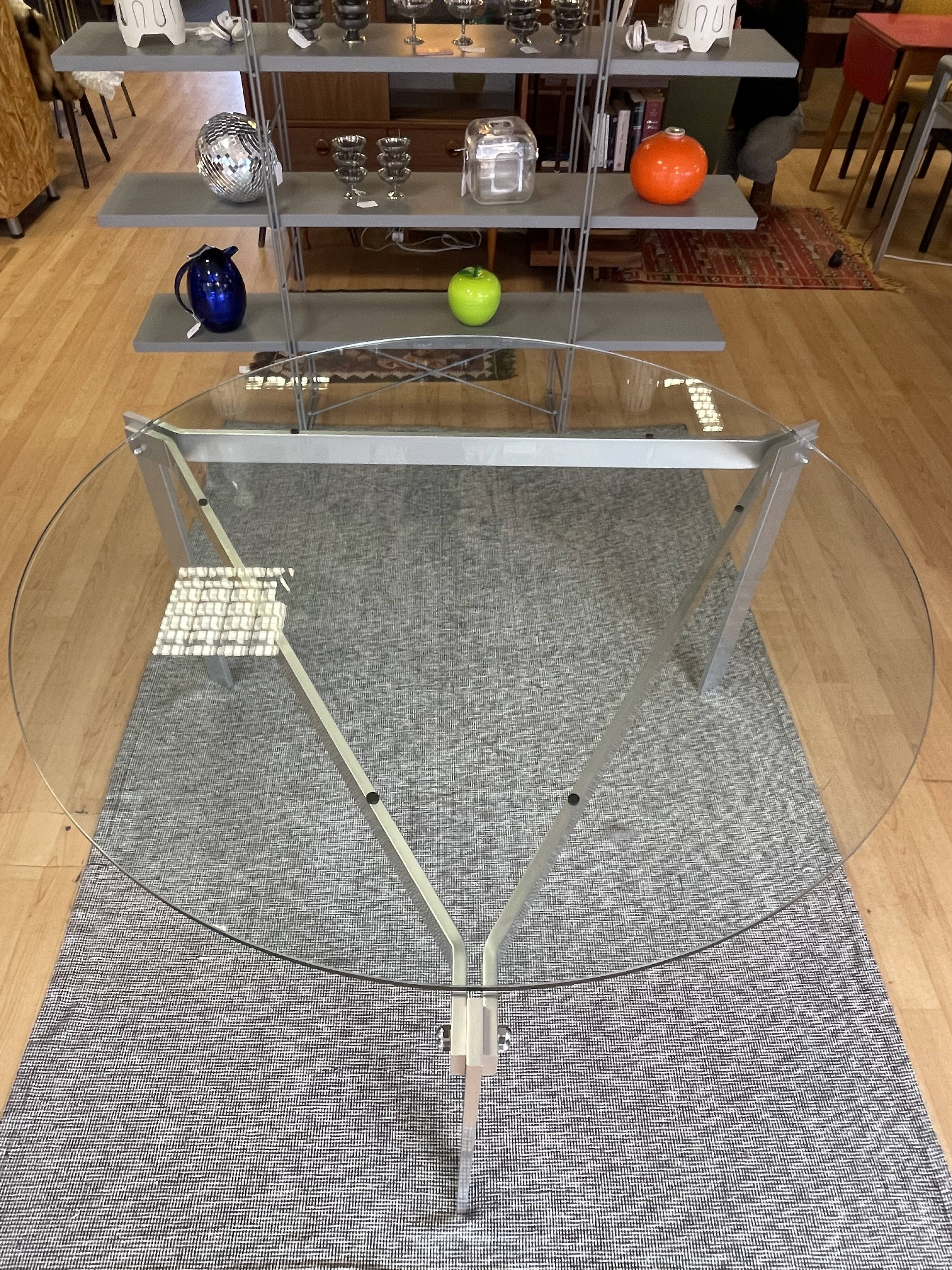 Round dining table with a glass top and brushed metal triangular frame.
