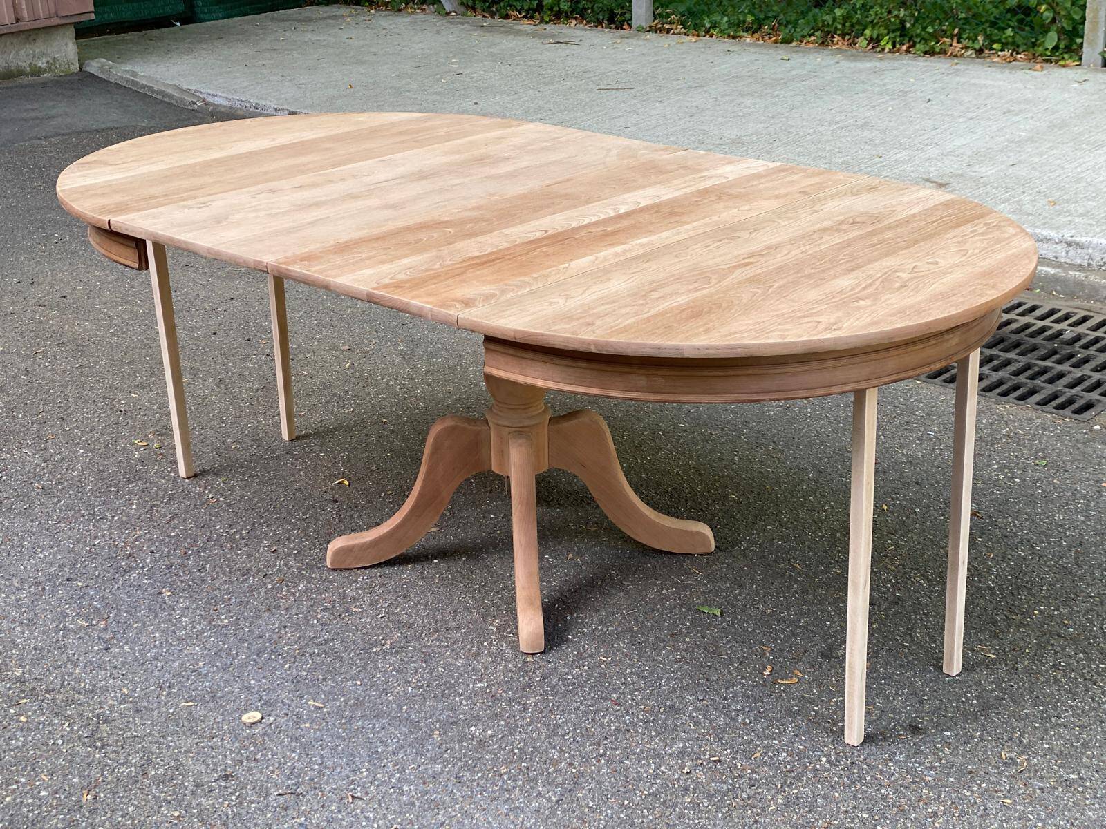 Large extendable round dining table stripped in solid cherry wood with a central leg.