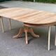 Large extendable round dining table stripped in solid cherry wood with a central leg.
