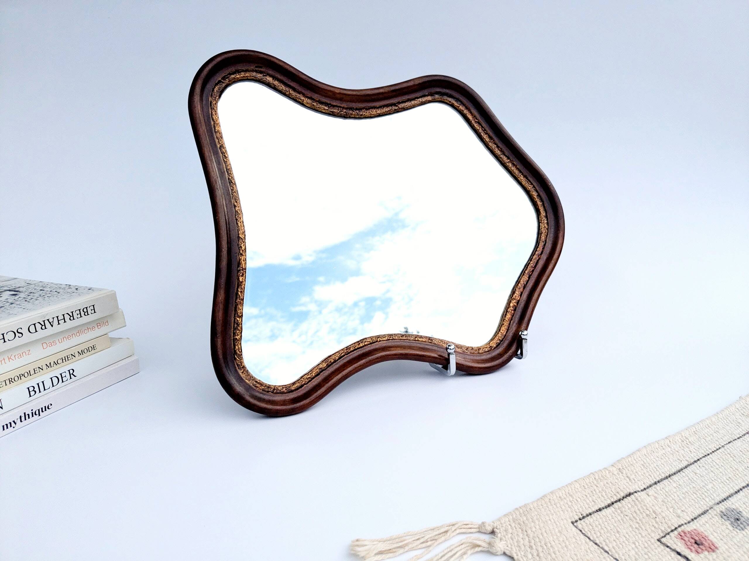 Antique wall mirror in carved wood with a wavy shape and a golden trim.