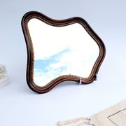 Antique wall mirror in carved wood with a wavy shape and a golden trim.