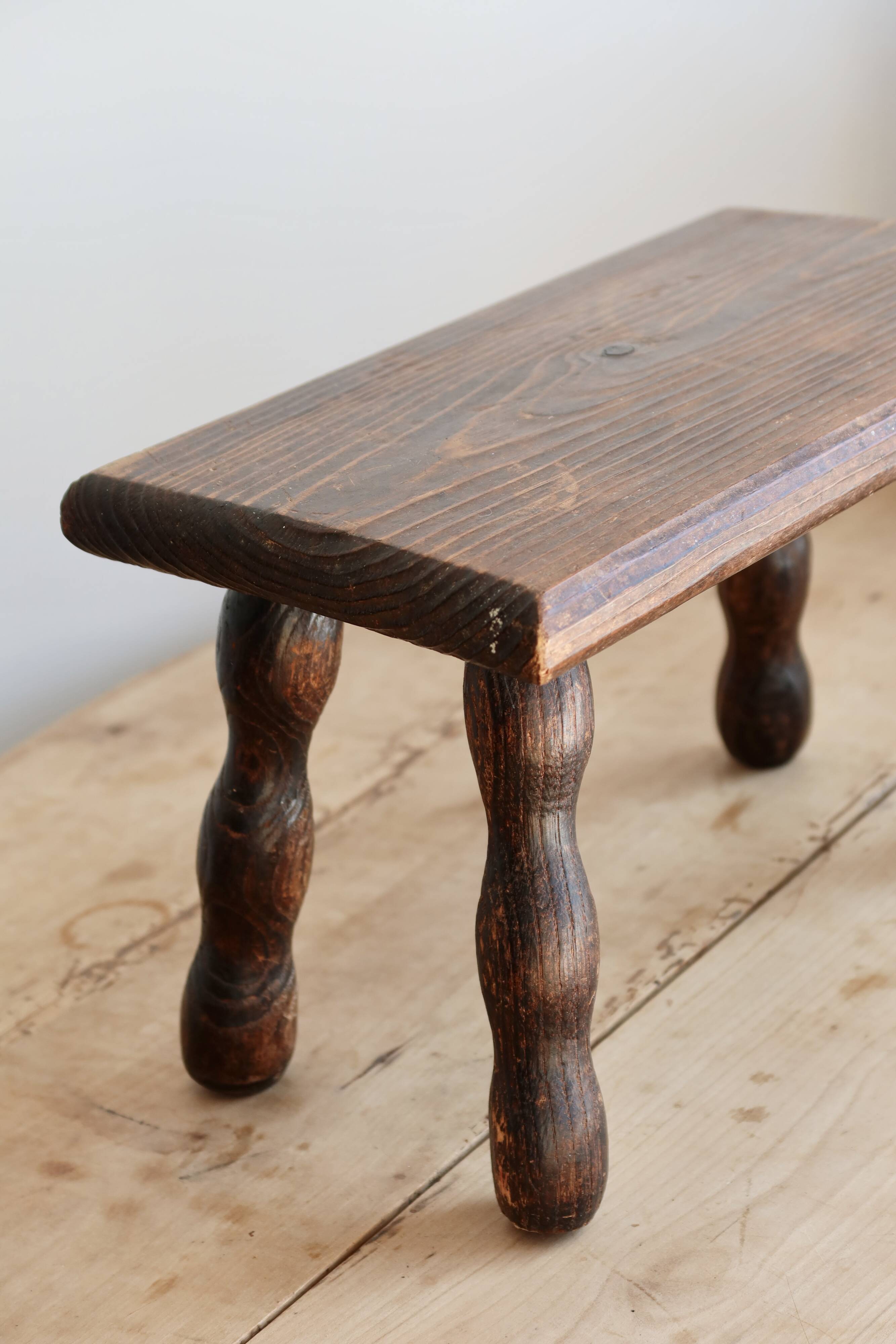 Vintage rectangular stool in dark wood with turned legs.