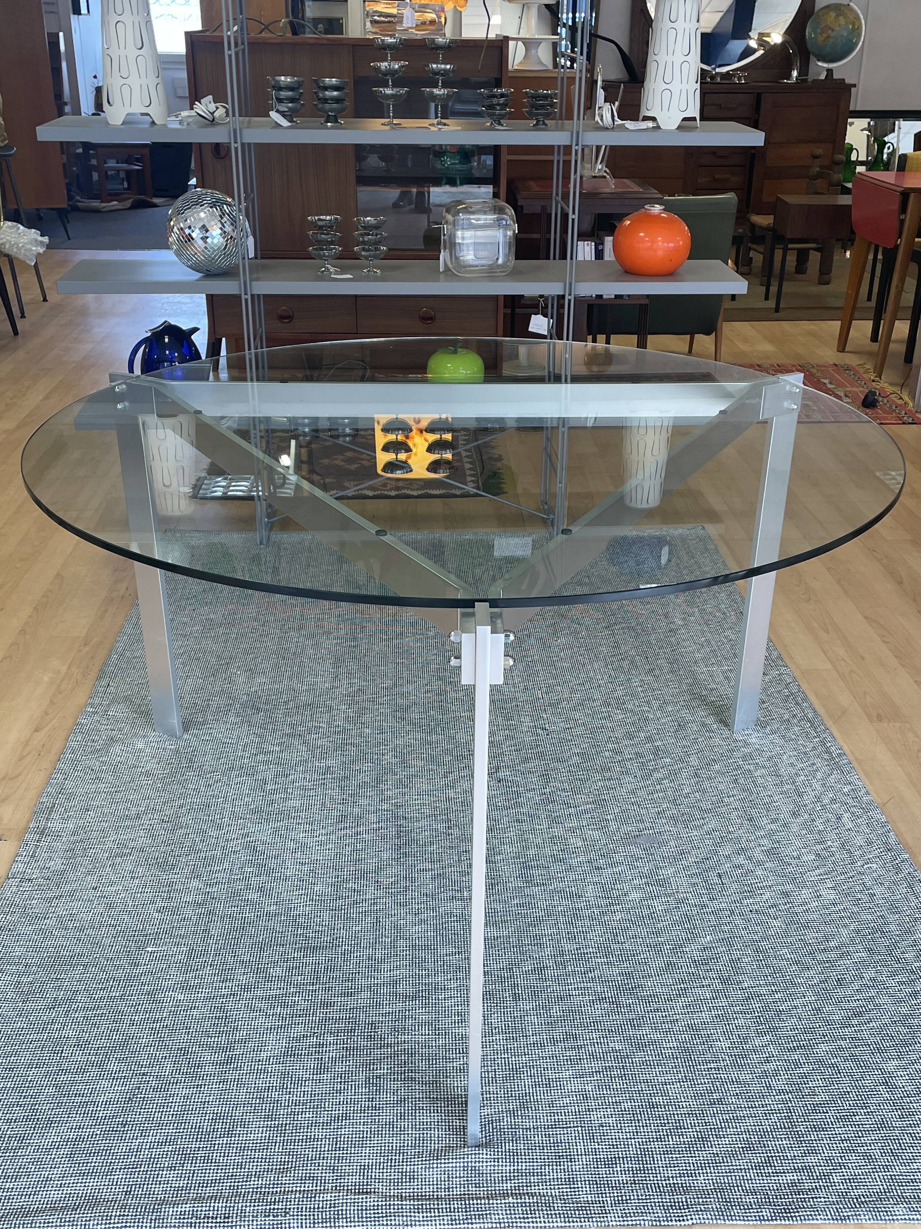Round dining table with a glass top and brushed metal triangular frame.