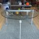 Round dining table with a glass top and brushed metal triangular frame.
