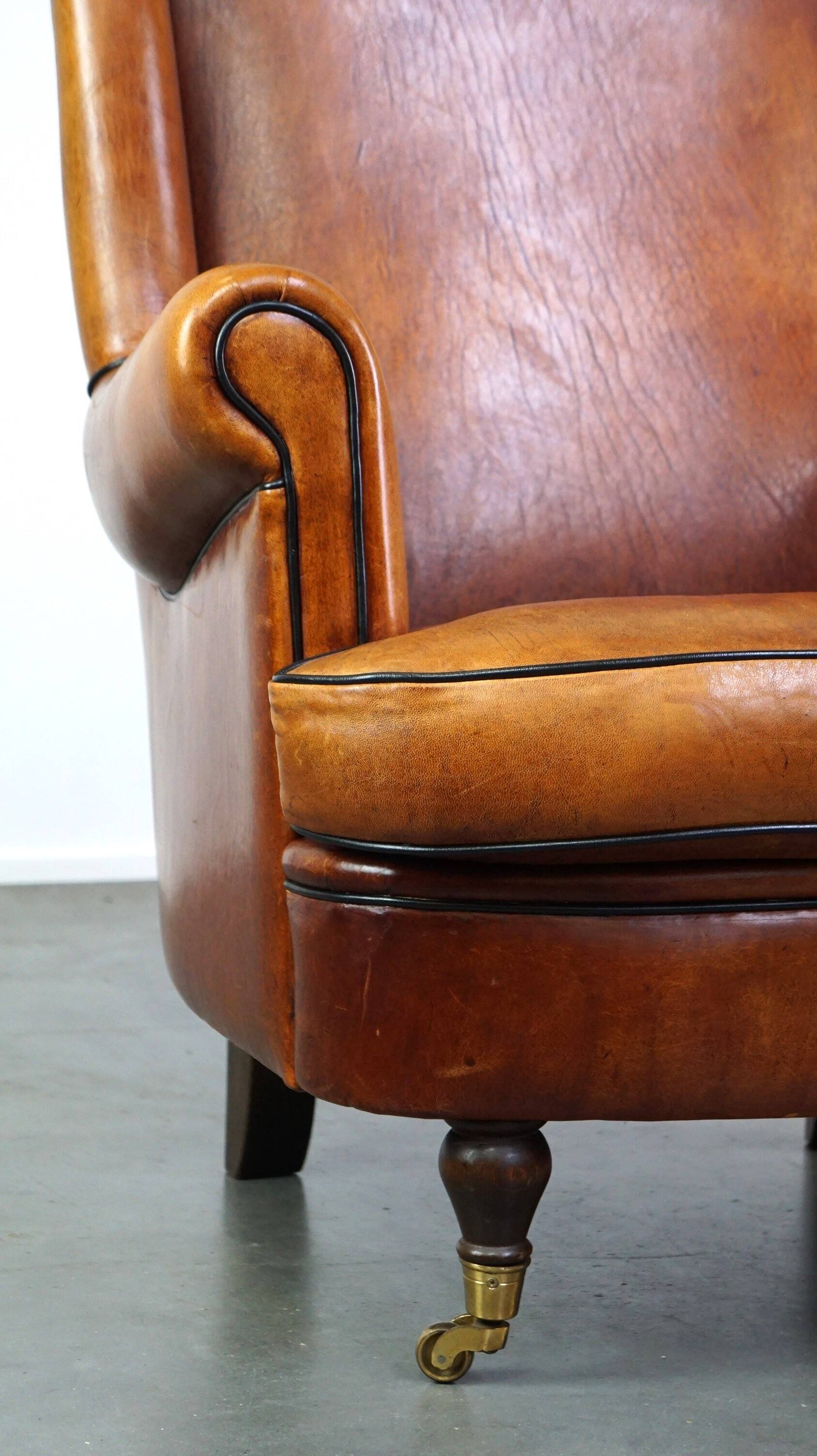 Subtle sheepskin wing chair in good condition on brass front wheels