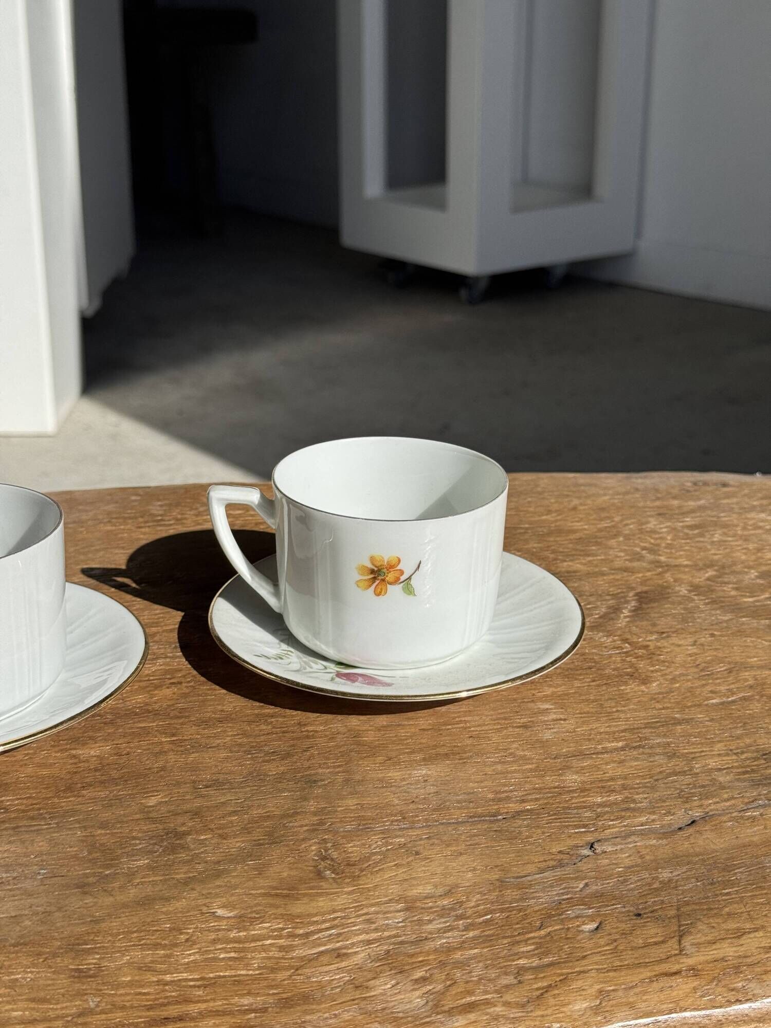 Pair of white porcelain cups from ADP France with a floral pattern and their s