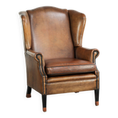 Fauteuil à oreilles en peau de mouton avec patine, fini avec des clous décoratifs.