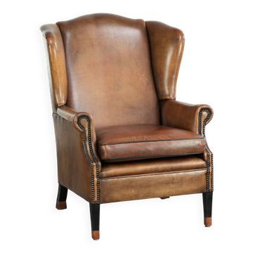 Fauteuil à oreilles en peau de mouton avec patine, fini avec des clous décoratifs.