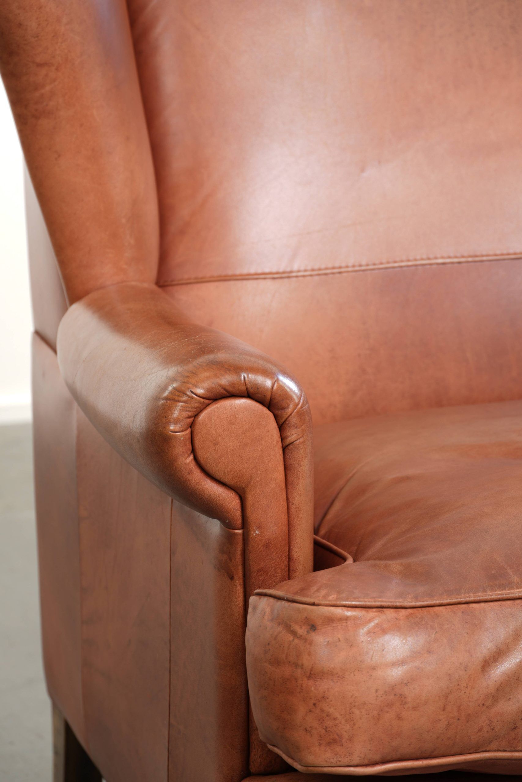 Light cognac-coloured cow leather wingback armchair with matching piping