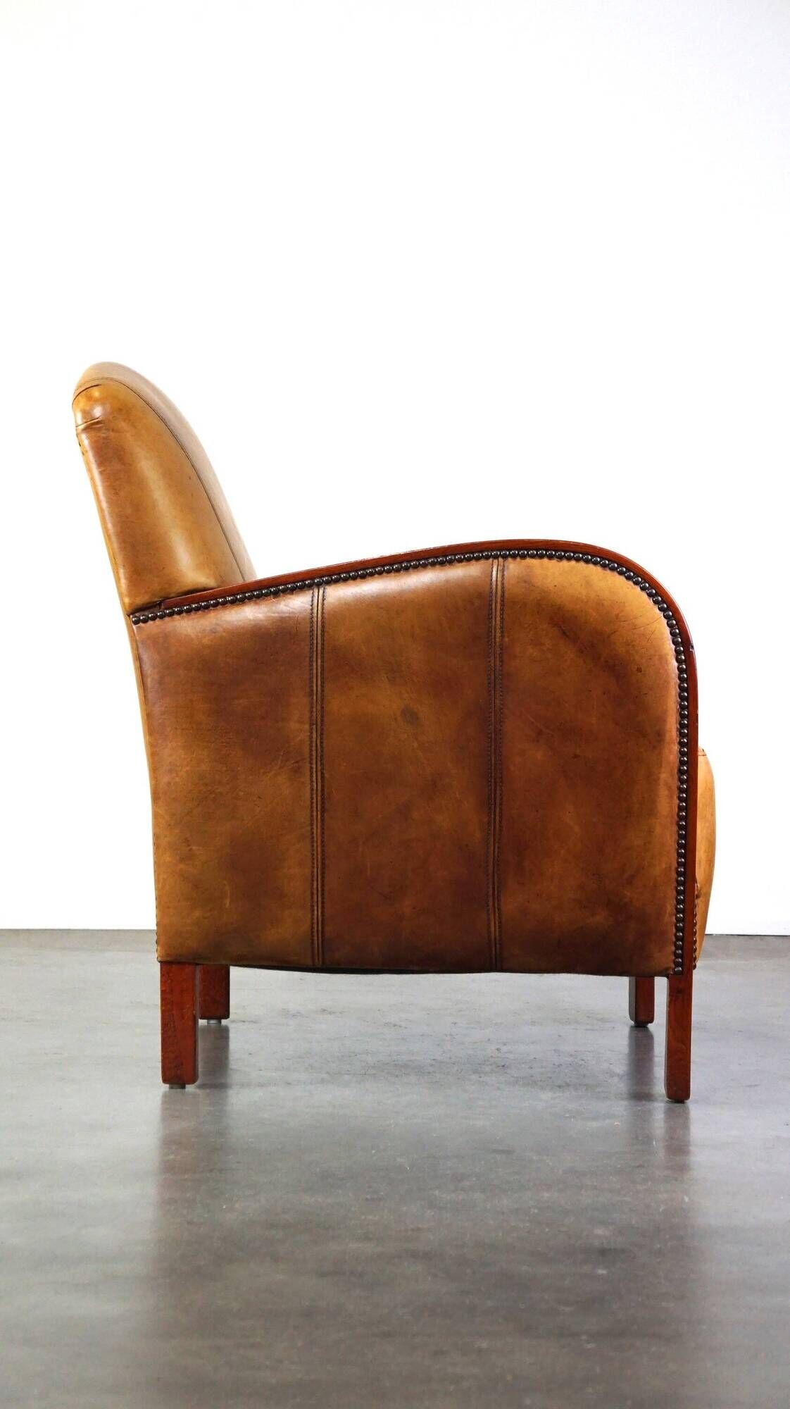 Luxurious cowhide Art Deco design armchair with wooden armrests and cognac-colored leather