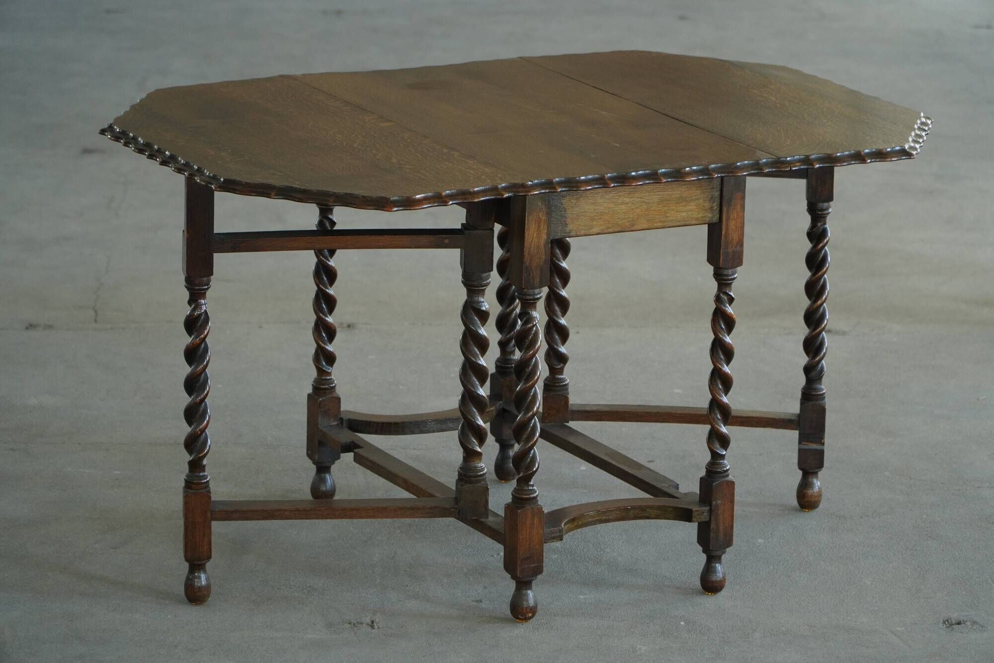 Antique baroque dining table in oak, with folding legs and drop leaves, featuring spiral "barley twist" legs, from the 1920s.