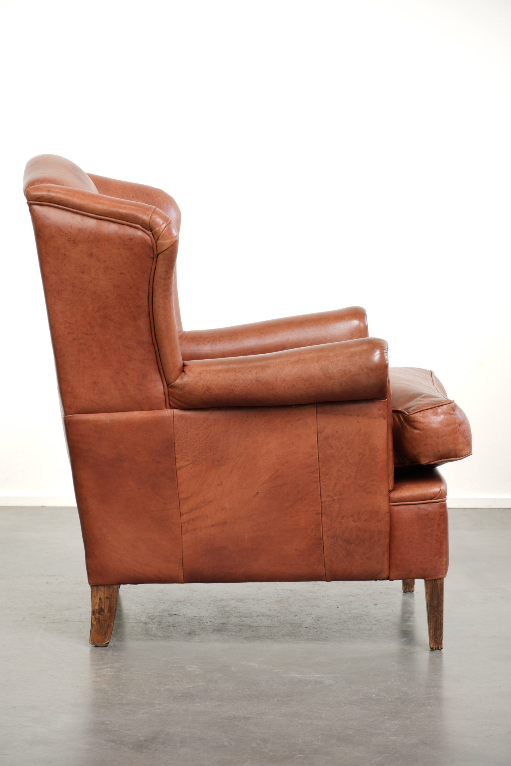Light cognac-coloured cow leather wingback armchair with matching piping