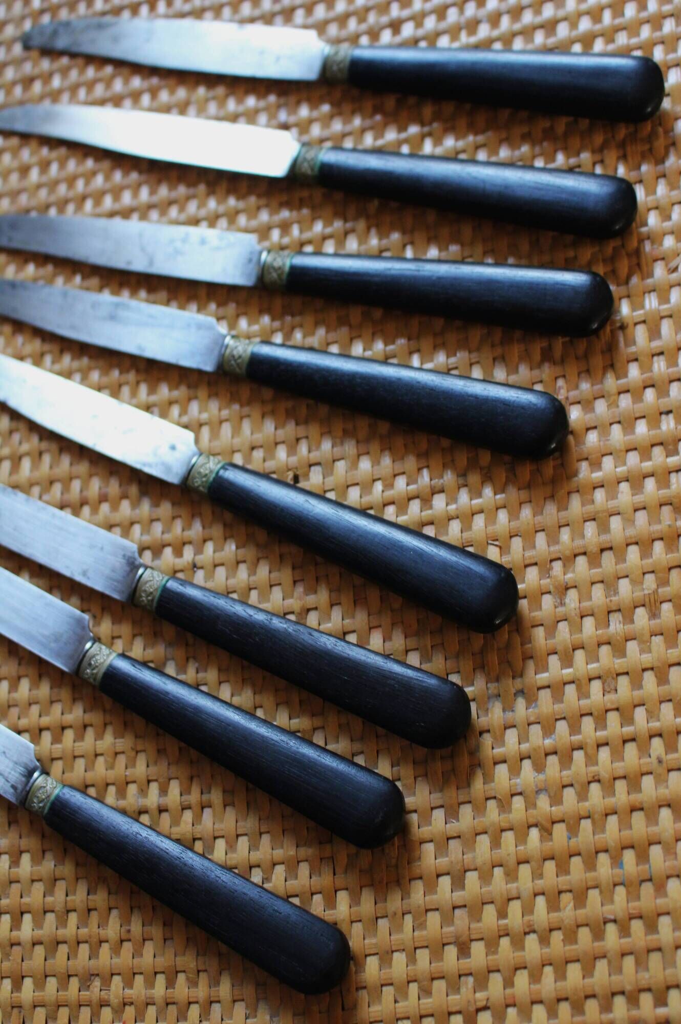 A set of 8 knives with black wooden handles and bolsters.