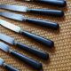 A set of 8 knives with black wooden handles and bolsters.
