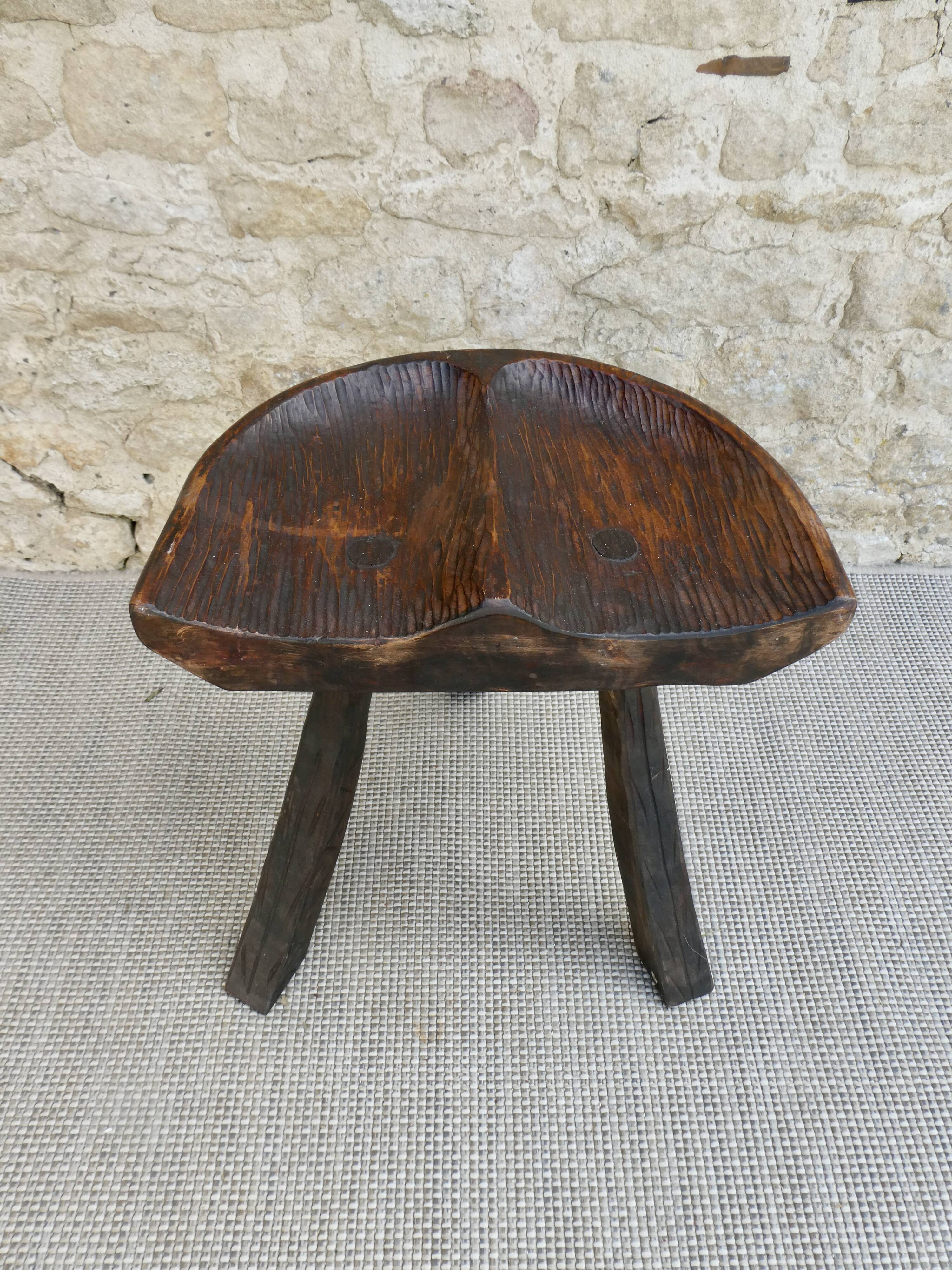 Tripod stool made of solid wood, with a carved seat.