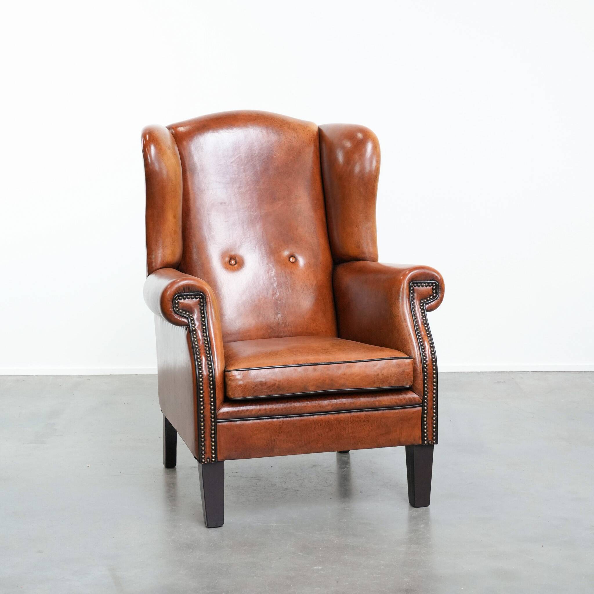 Large sheepskin wingback chair with black piping and decorative nails