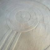 Round ecru rug with geometric relief patterns in wool