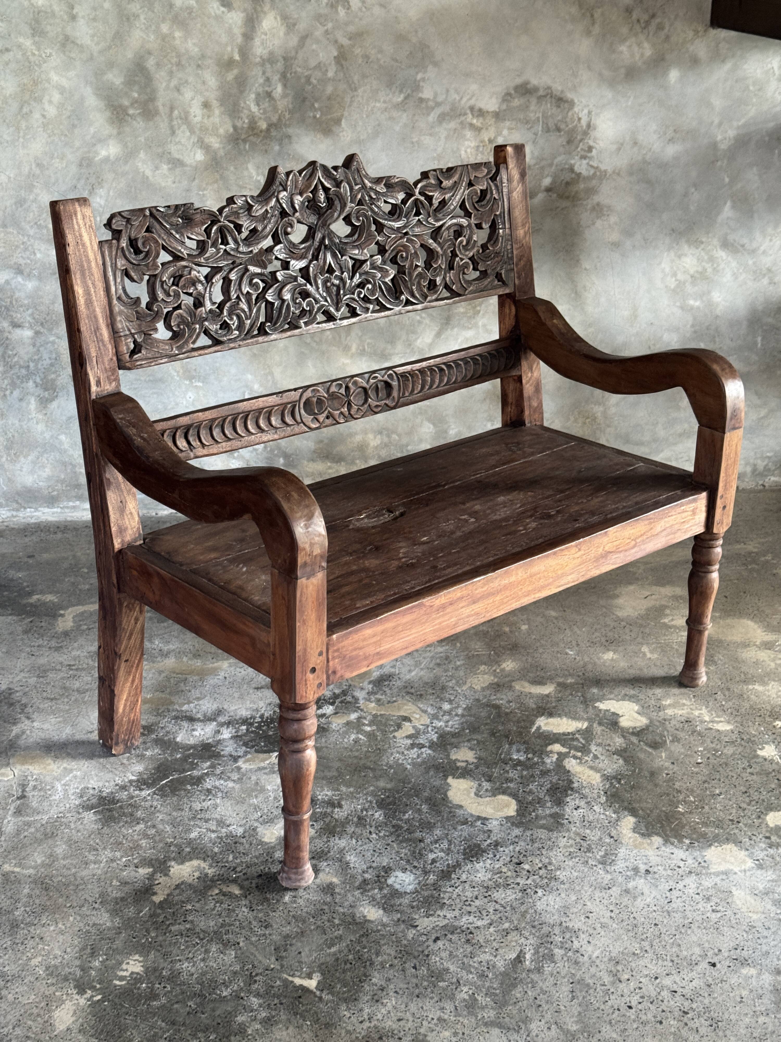 Small antique Indonesian bench in carved teak with plant and floral motifs.