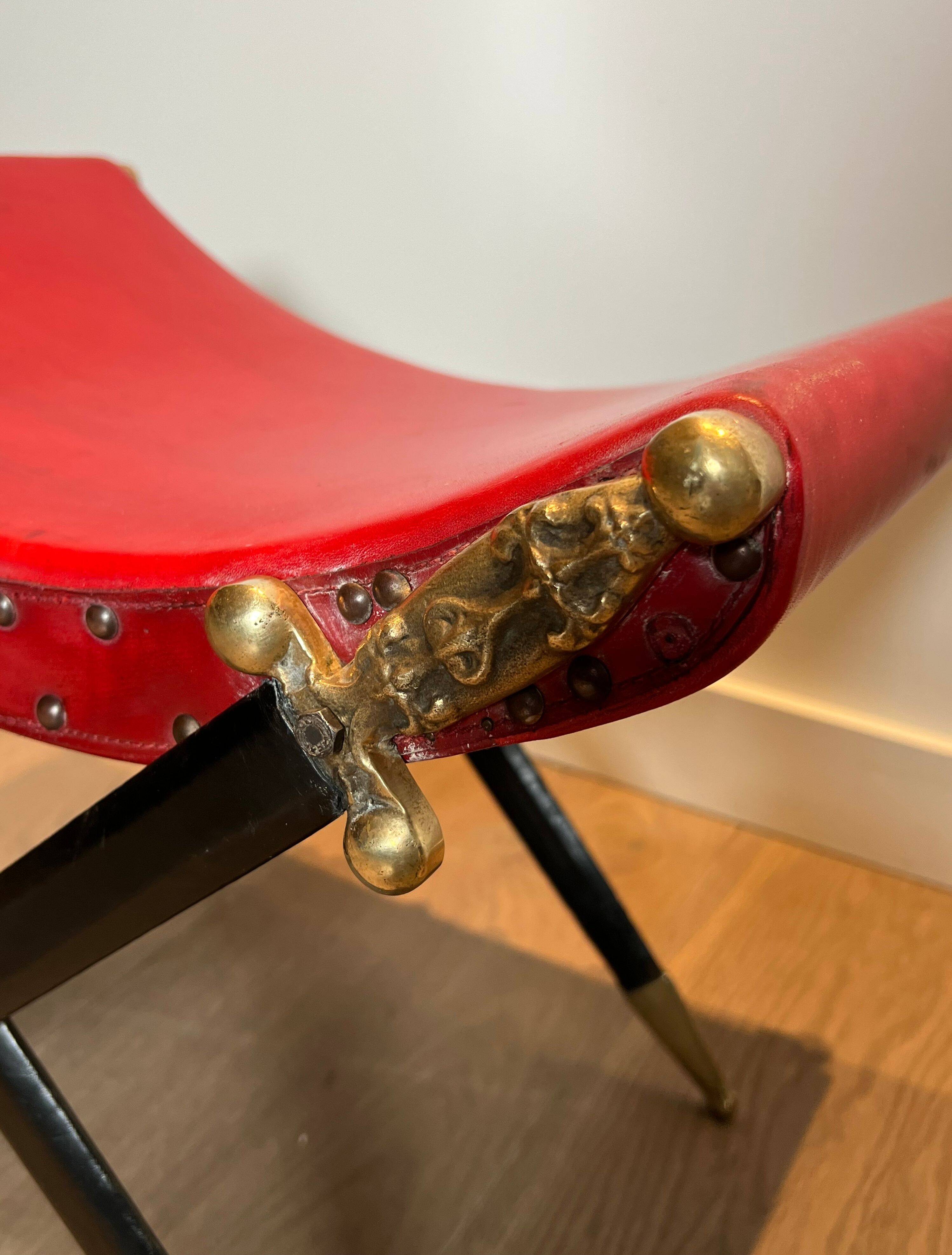 Neoclassical curule stool in red leather, decorated with crossed swords in bronze and metal covered in black leather.