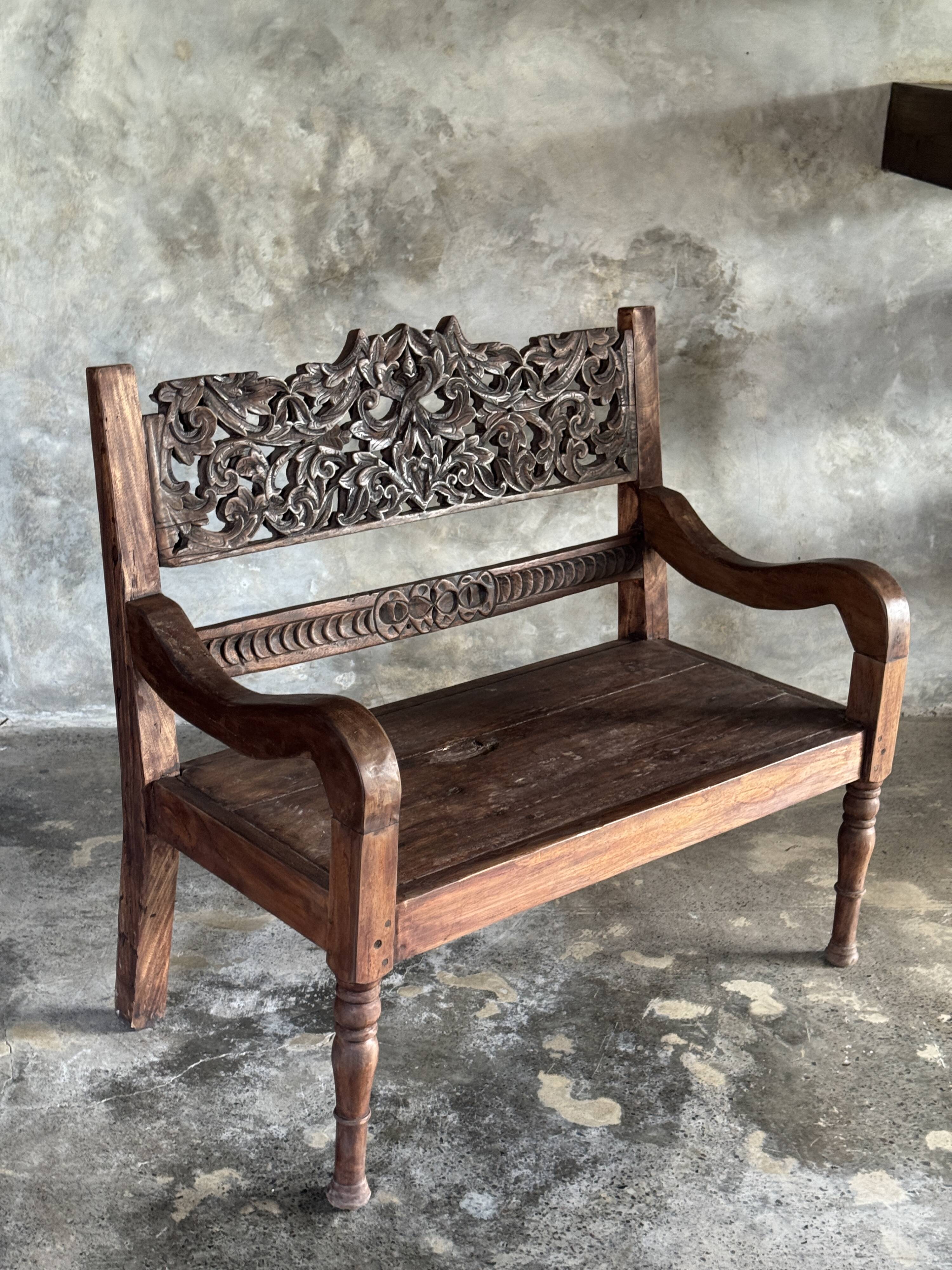 Small antique Indonesian bench in carved teak with plant and floral motifs.