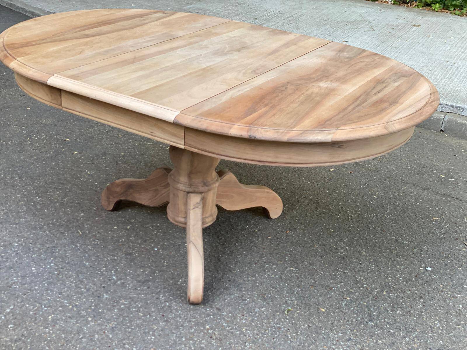 Round extendable dining table stripped in solid raw walnut with a central leg.