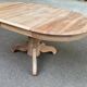 Round extendable dining table stripped in solid raw walnut with a central leg.