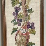 Broderie hollandaise encadrée représentant une vigne avec des raisins, des bouteilles de vin et des paniers
