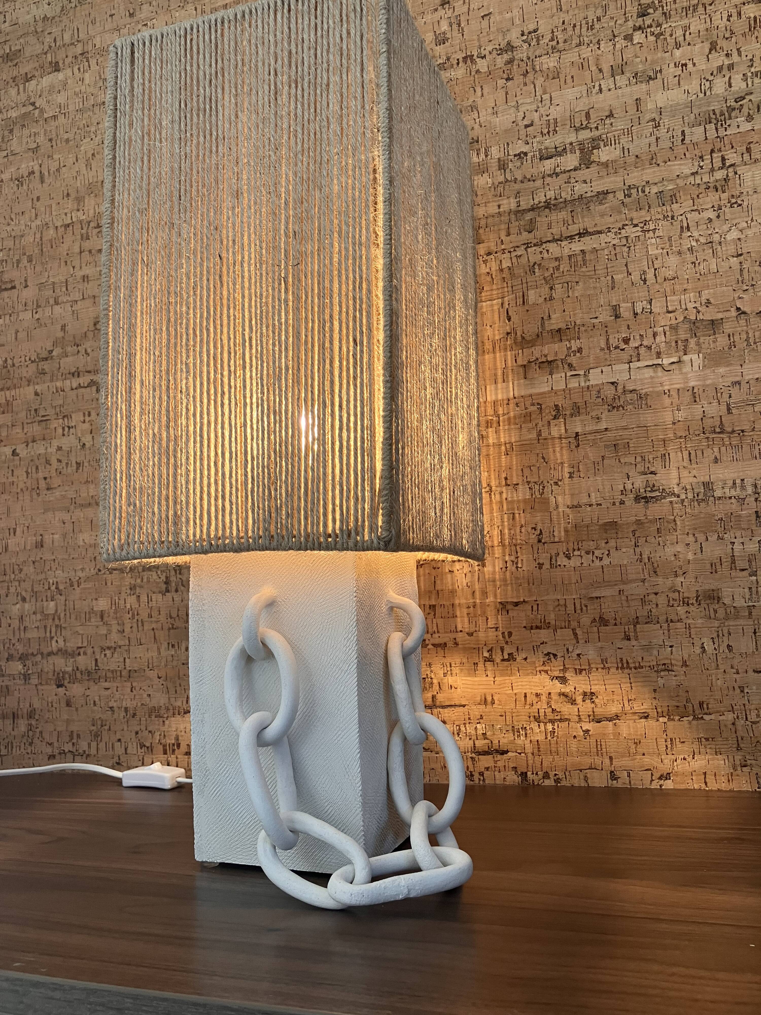 Table lamp in ceramic with decorative chain and cord shade.
