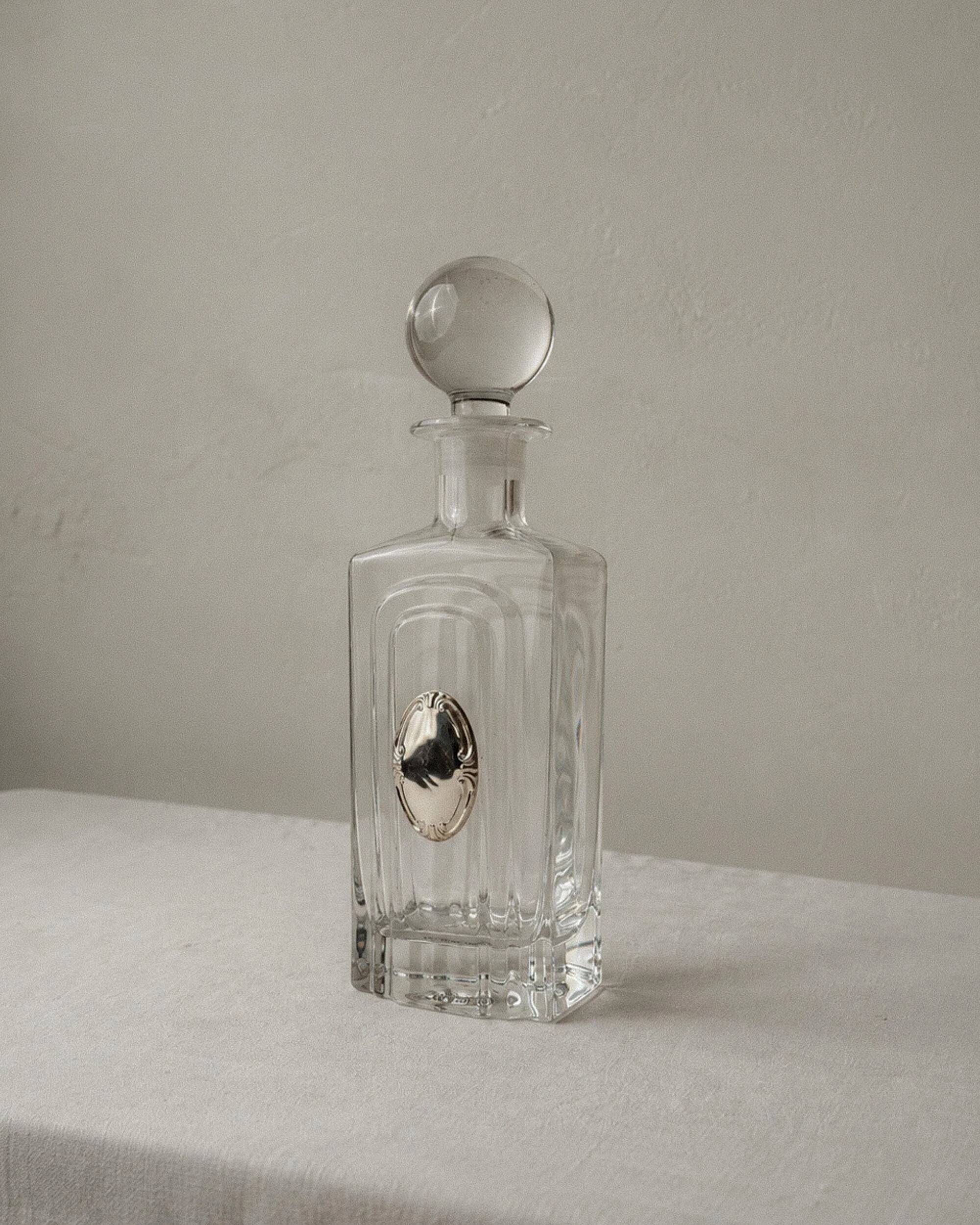Vintage glass decanter from the 1980s, transparent glass with a silver plate and spherical stopper.