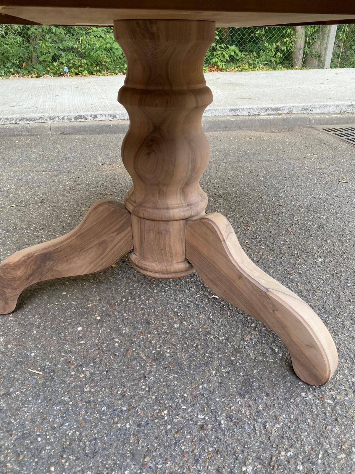 Round extendable dining table stripped in solid raw walnut with a central leg.