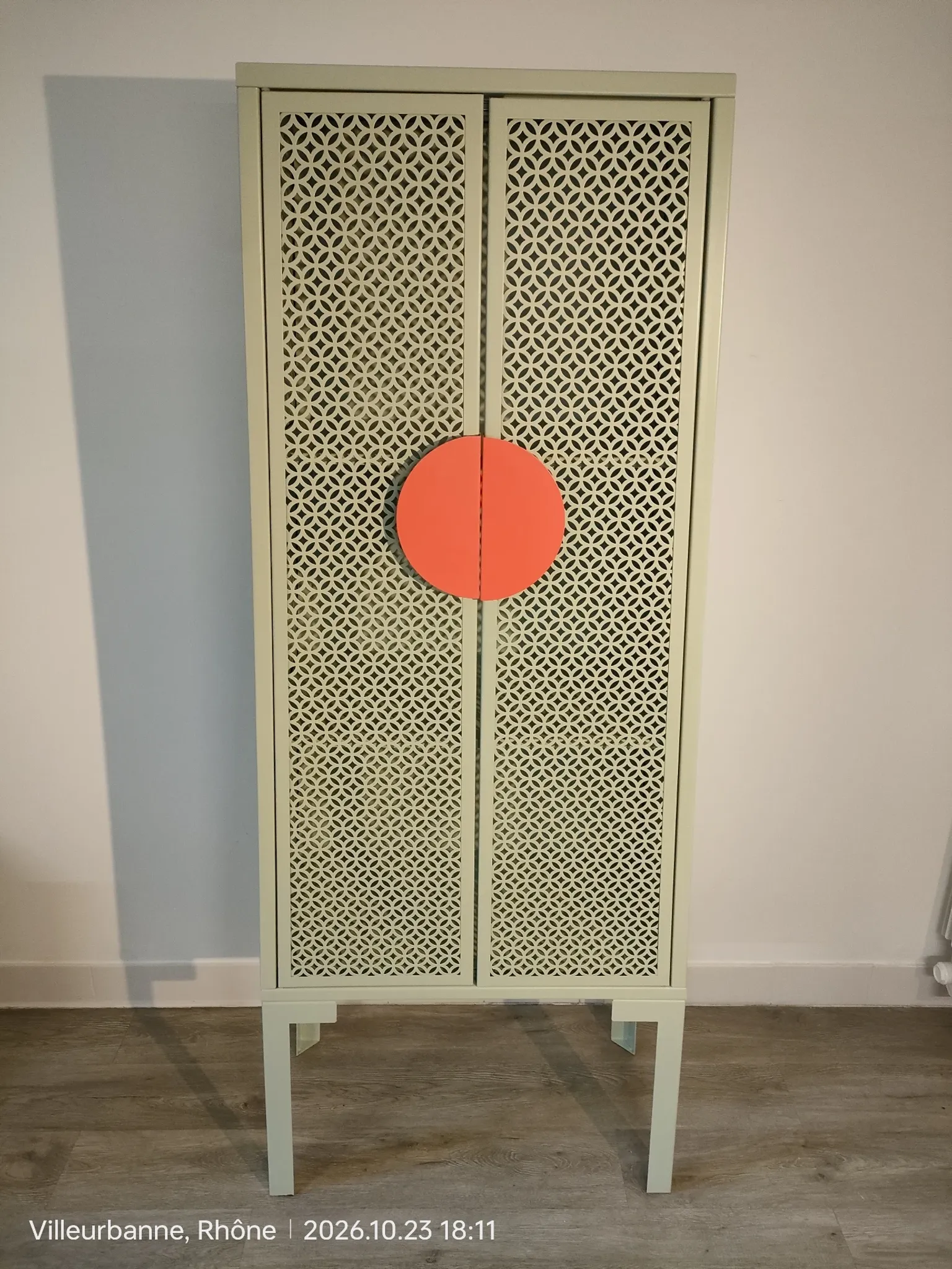 Vintage sage green metal wardrobe with louvered doors and coral handles.