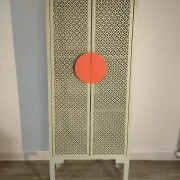 Vintage sage green metal wardrobe with louvered doors and coral handles.