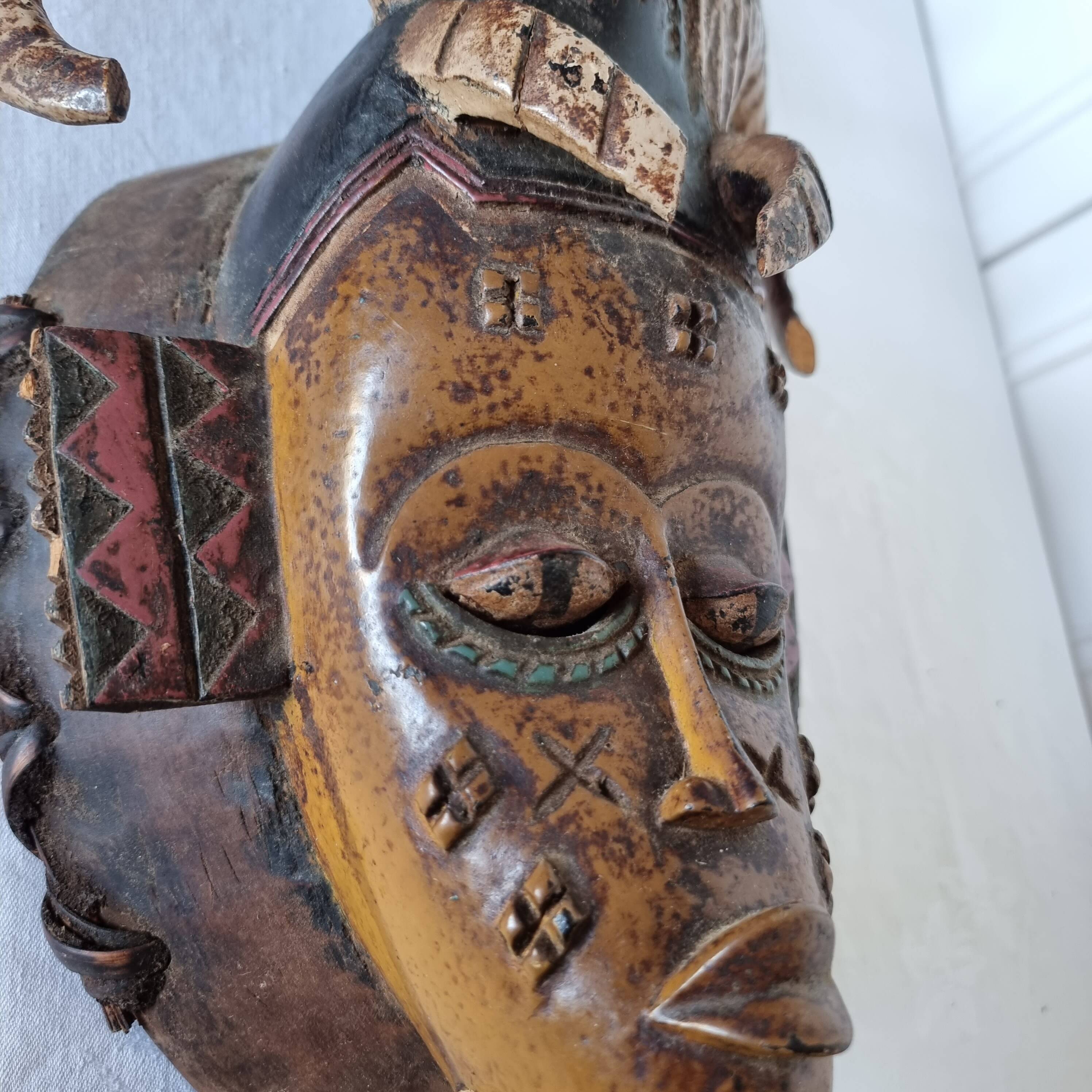 A large Senufo mask made of colored wood, decorated with an anthropomorphic figure