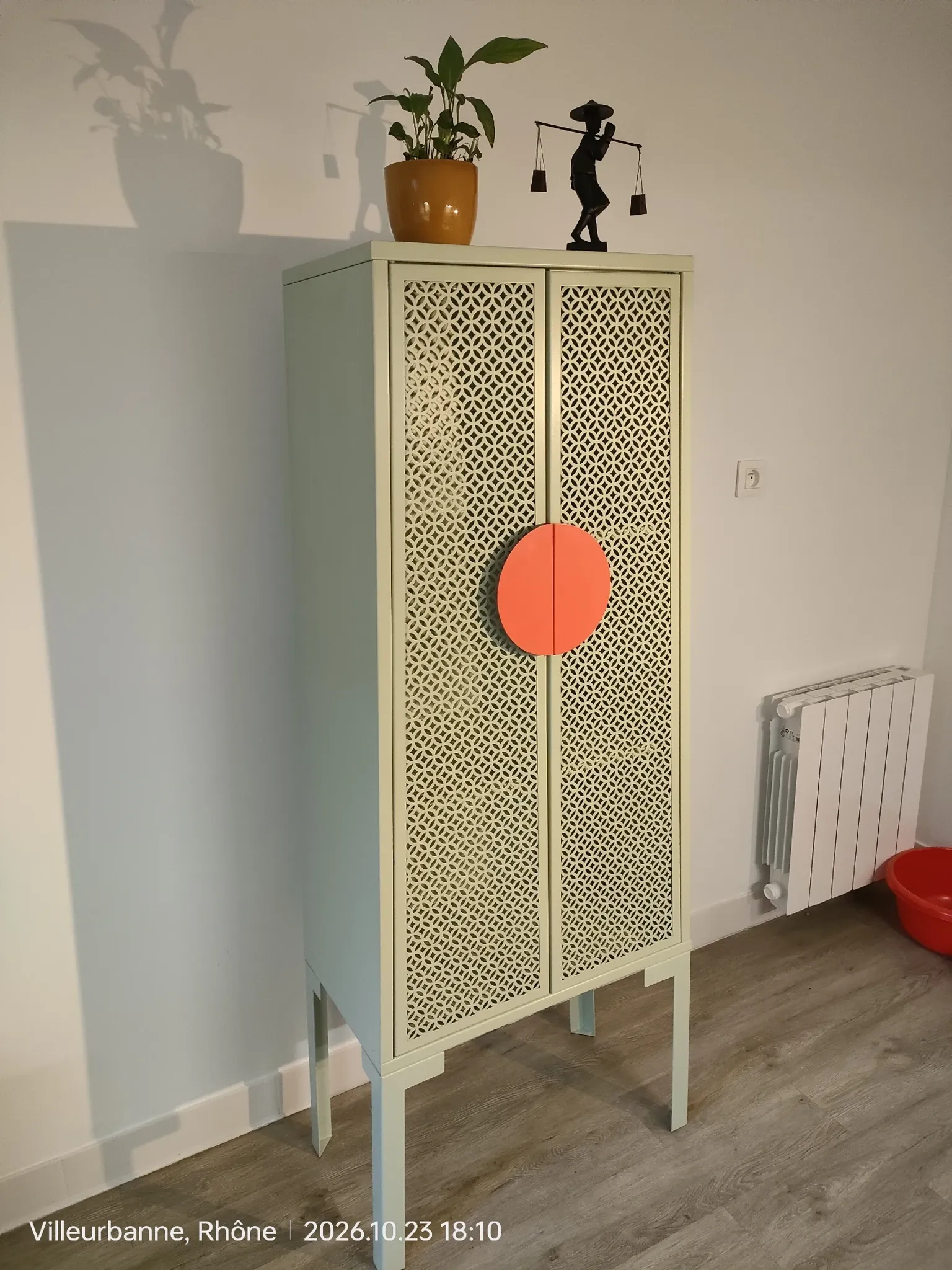 Vintage sage green metal wardrobe with louvered doors and coral handles.
