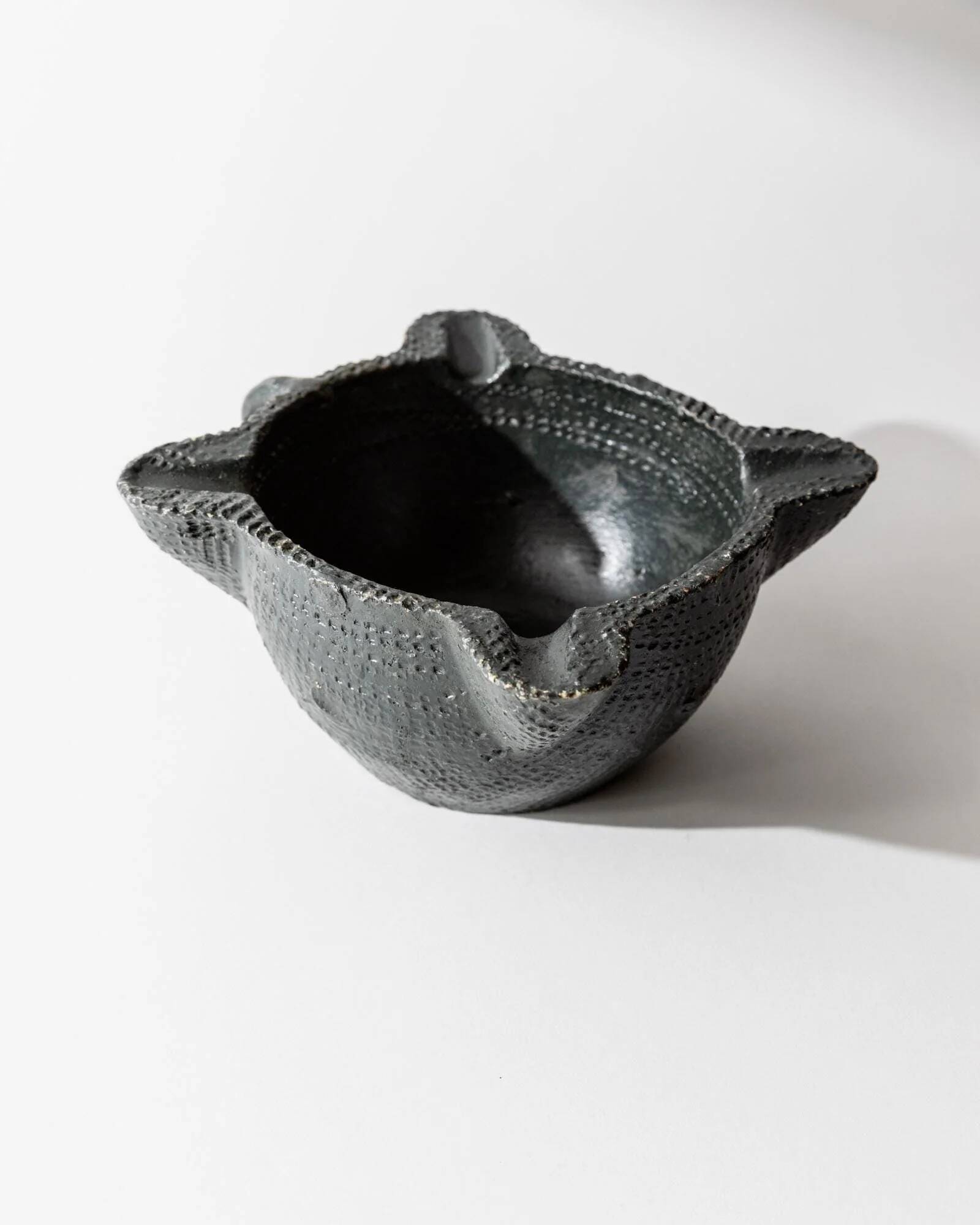 Vintage ceramic ashtray from the 1960s, black, hand-sculpted texture, organic shape.