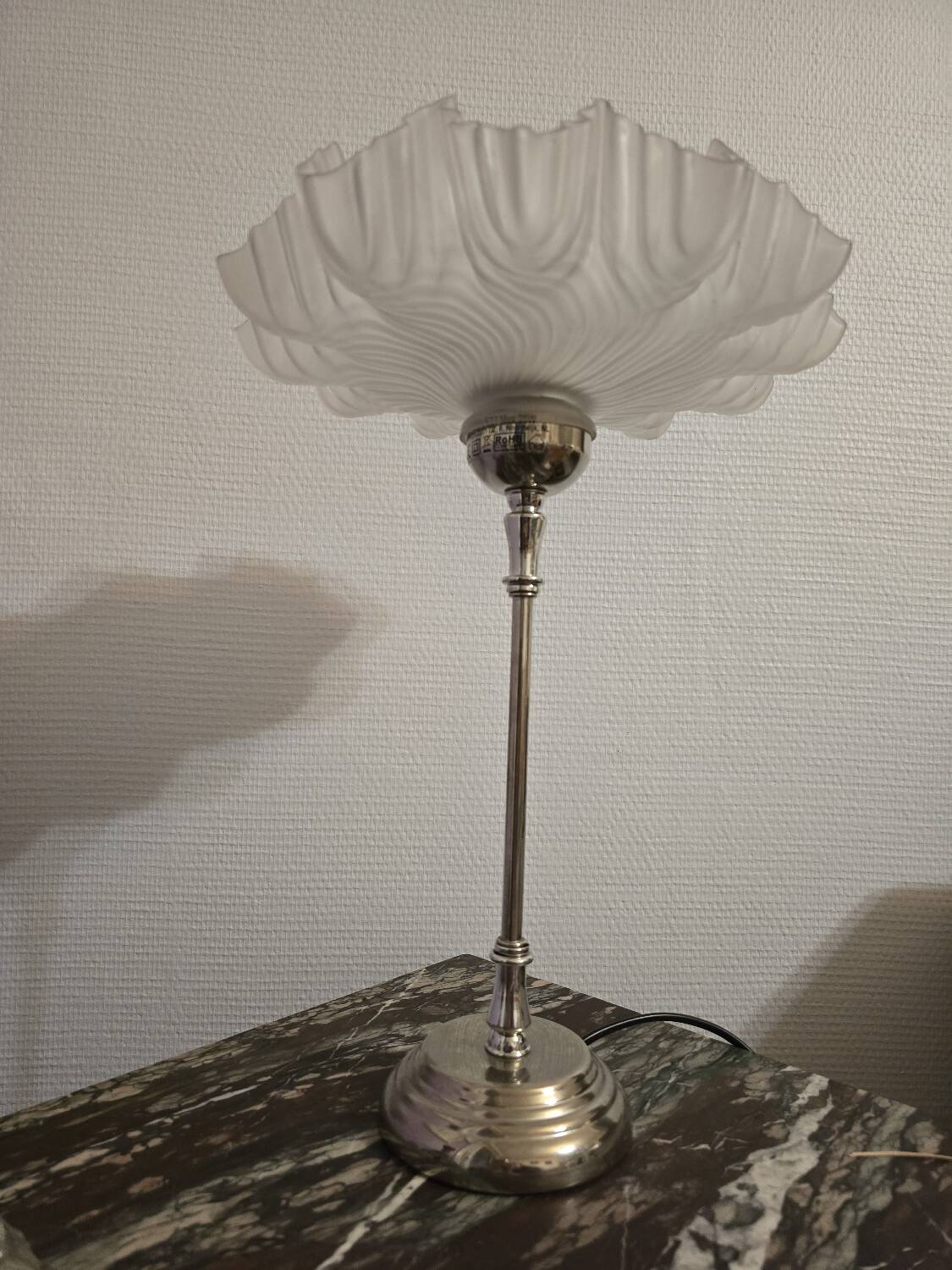 Table lamp with a silver base and a scalloped shade.