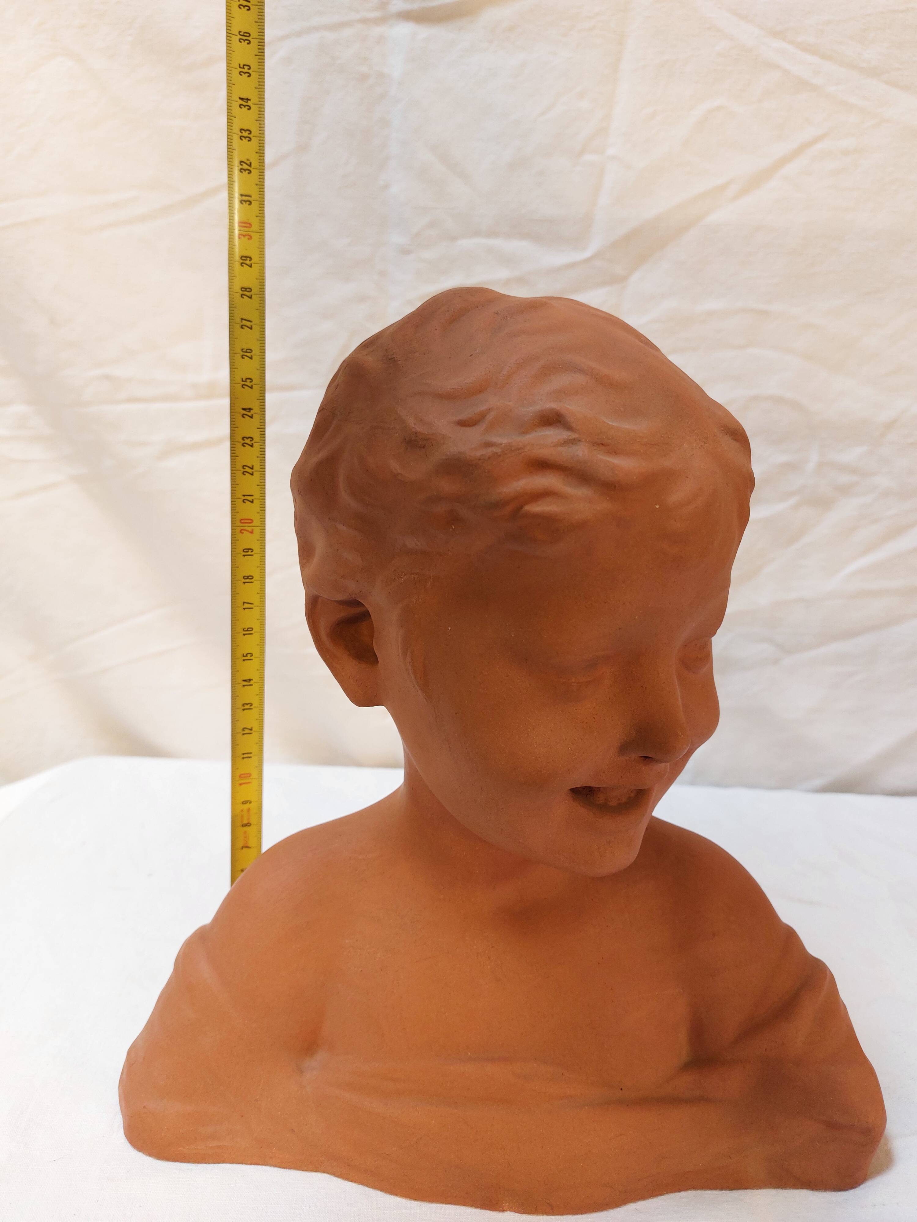 Terracotta bust of a smiling little boy.