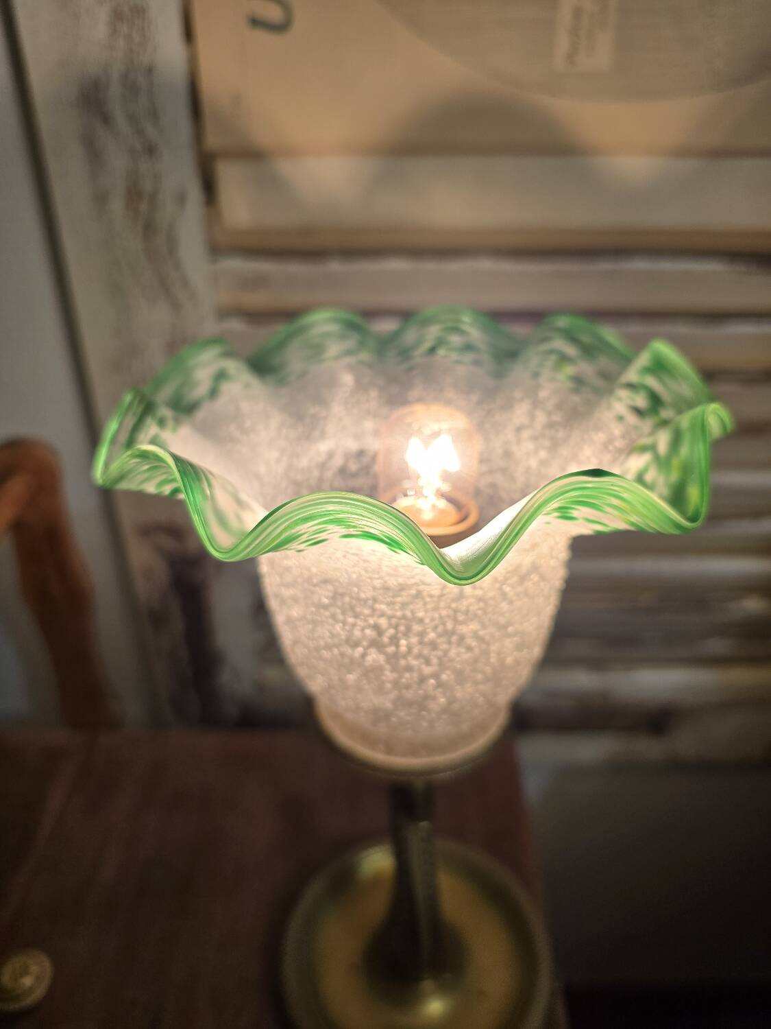 Small table lamp with a brass fish base and a tulip shade with green edges.