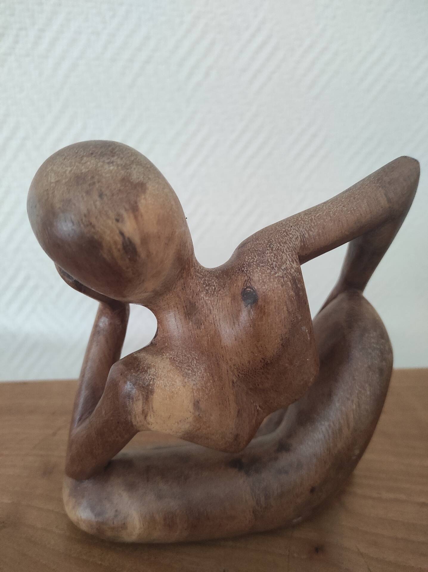 Wooden sculpted statuette of a woman in a pensive pose.