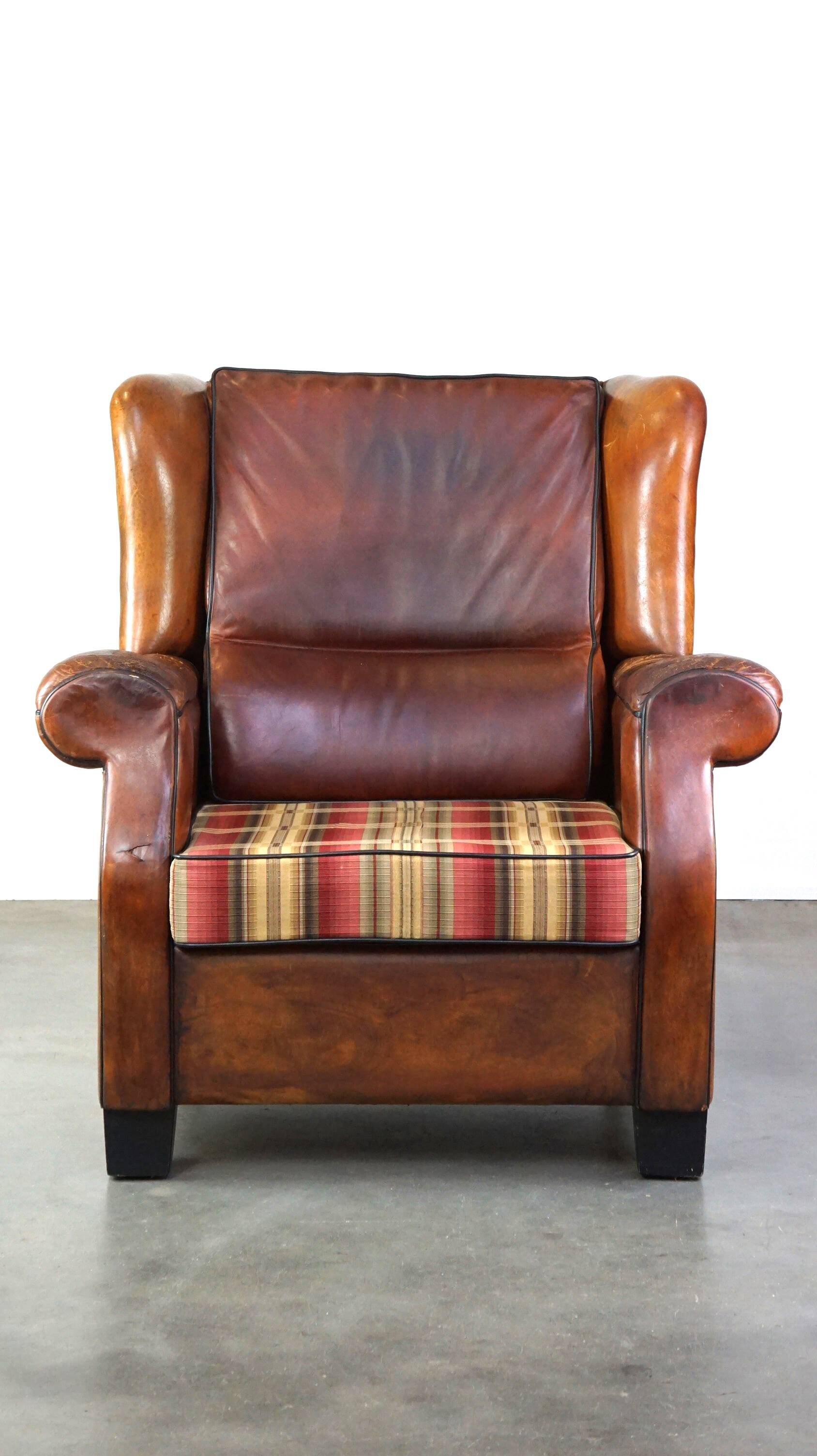 Very large worn sheepskin wing chair with a checked seat cushion