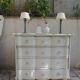 A beautifully crafted crossbow-shaped chest of drawers, finished in pearl grey with a whitewashed top.