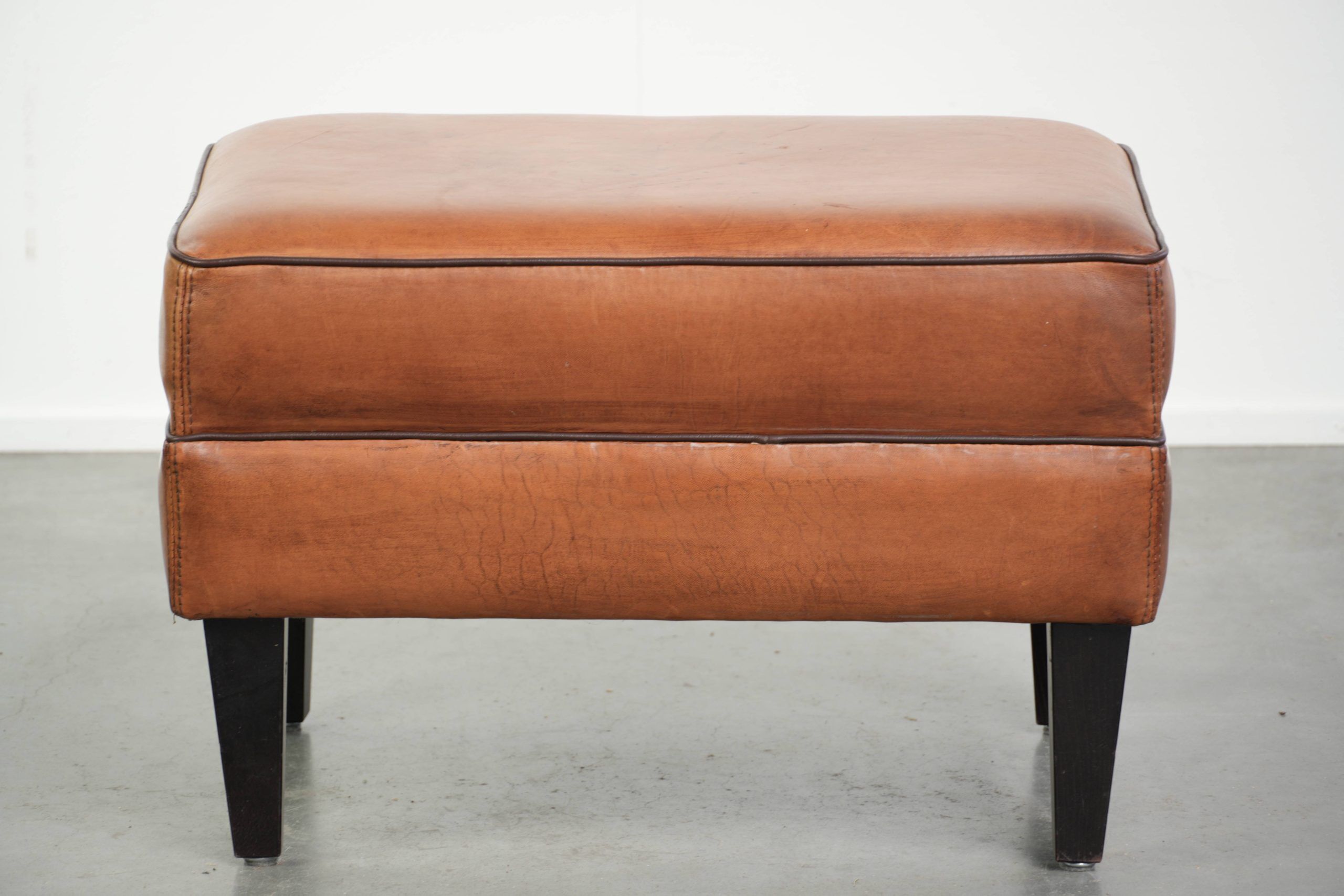 Handy sheepskin ottoman with warm colours finished with black piping