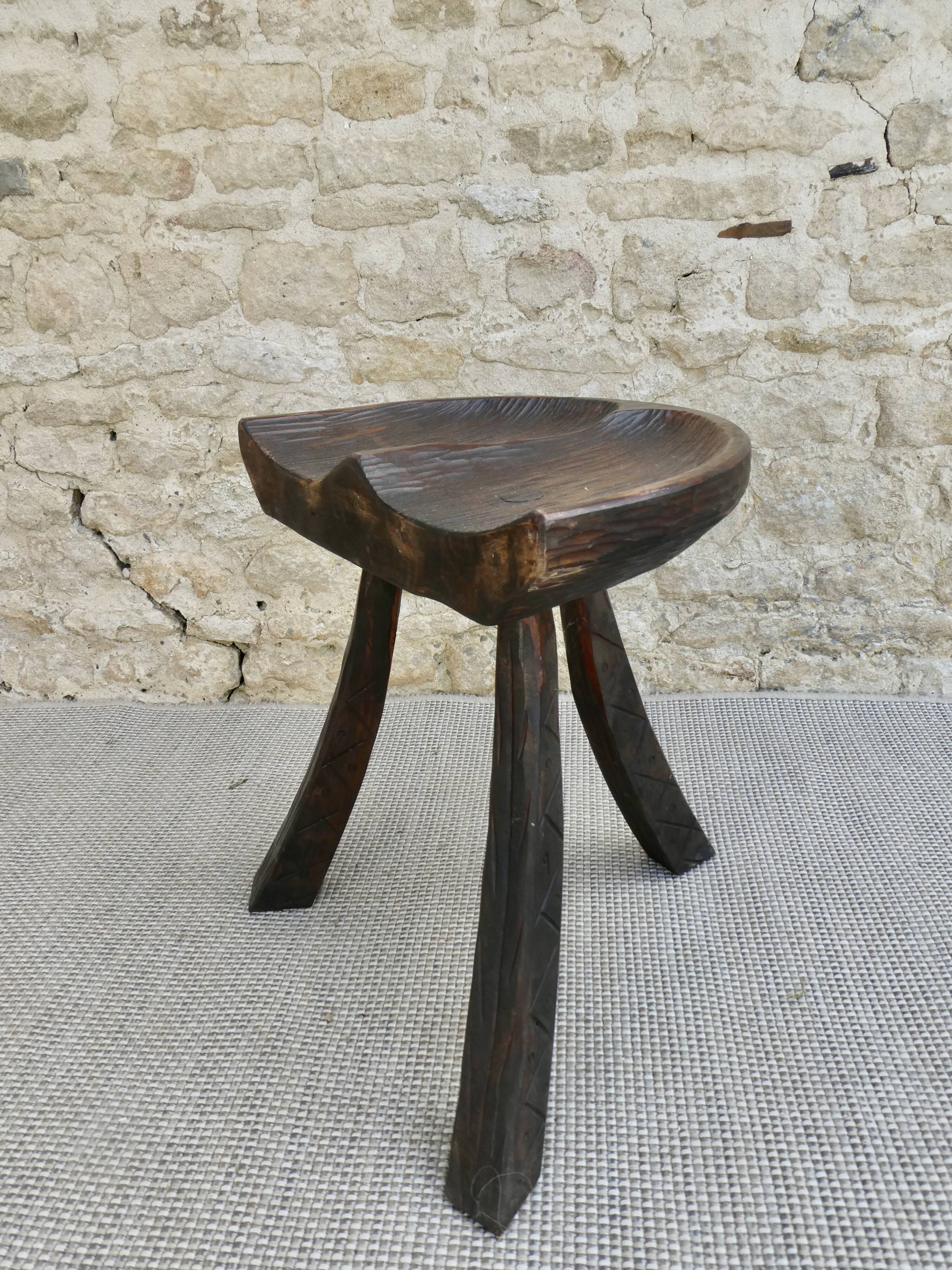Tripod stool made of solid wood, with a carved seat.